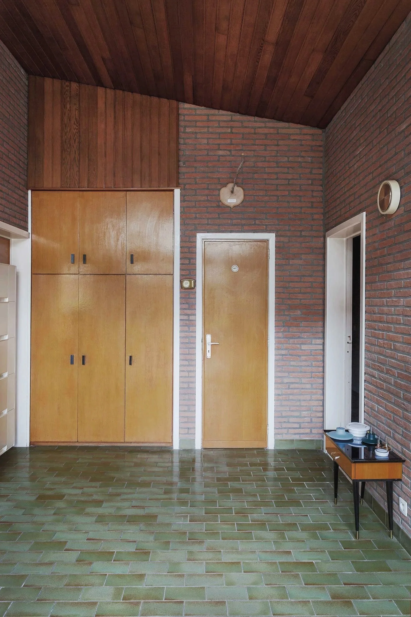 Interior of a vintage 70s home with green ceramic tiles, brick wall finishes, wooden doors, and integrated cabinetry.