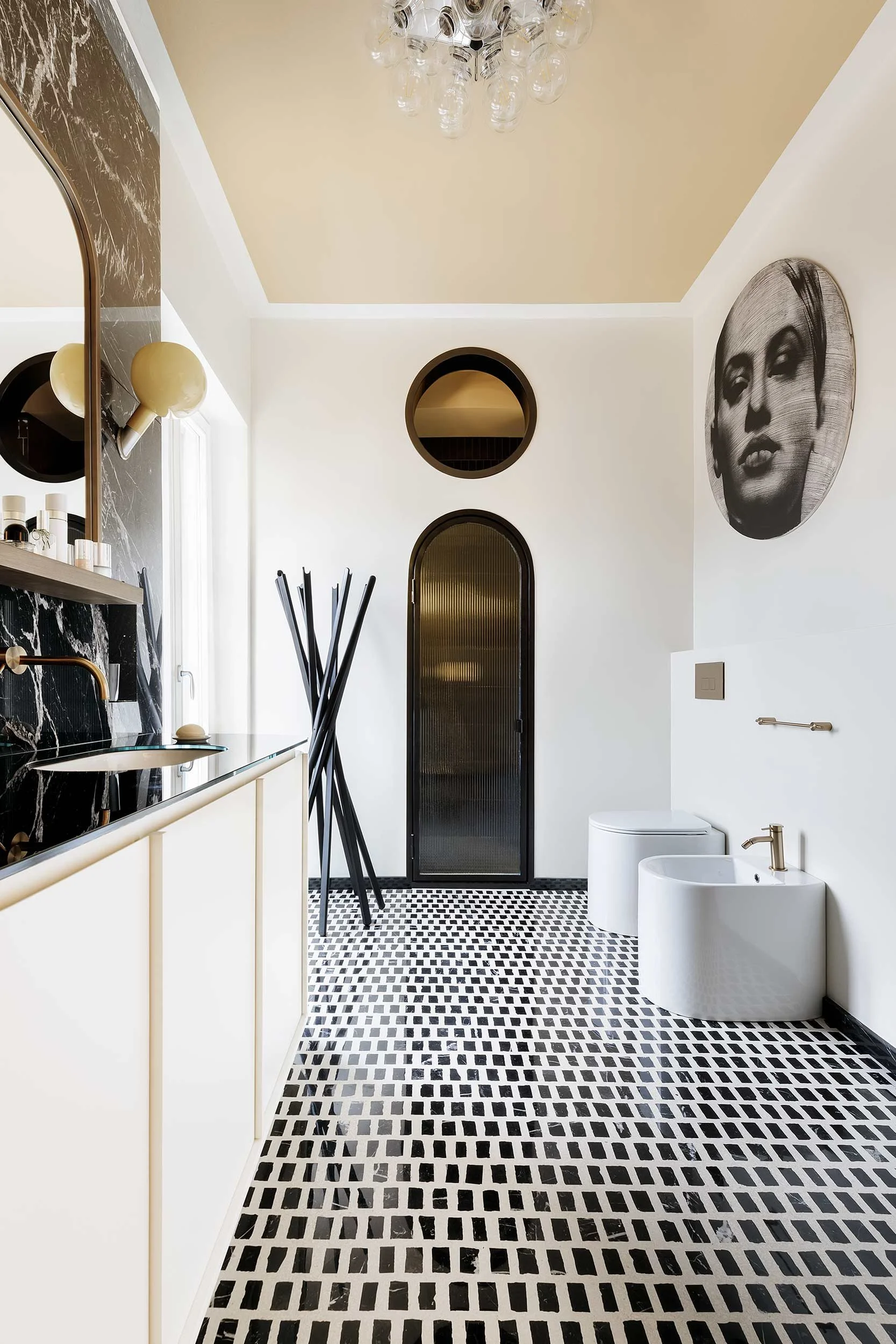 Bagno di design con richiami classici e moderni, caratterizzato da pavimento in mosaico bianco e nero, porta ad arco con finitura scura, sanitari contemporanei e lampada Parola di Fontana Arte