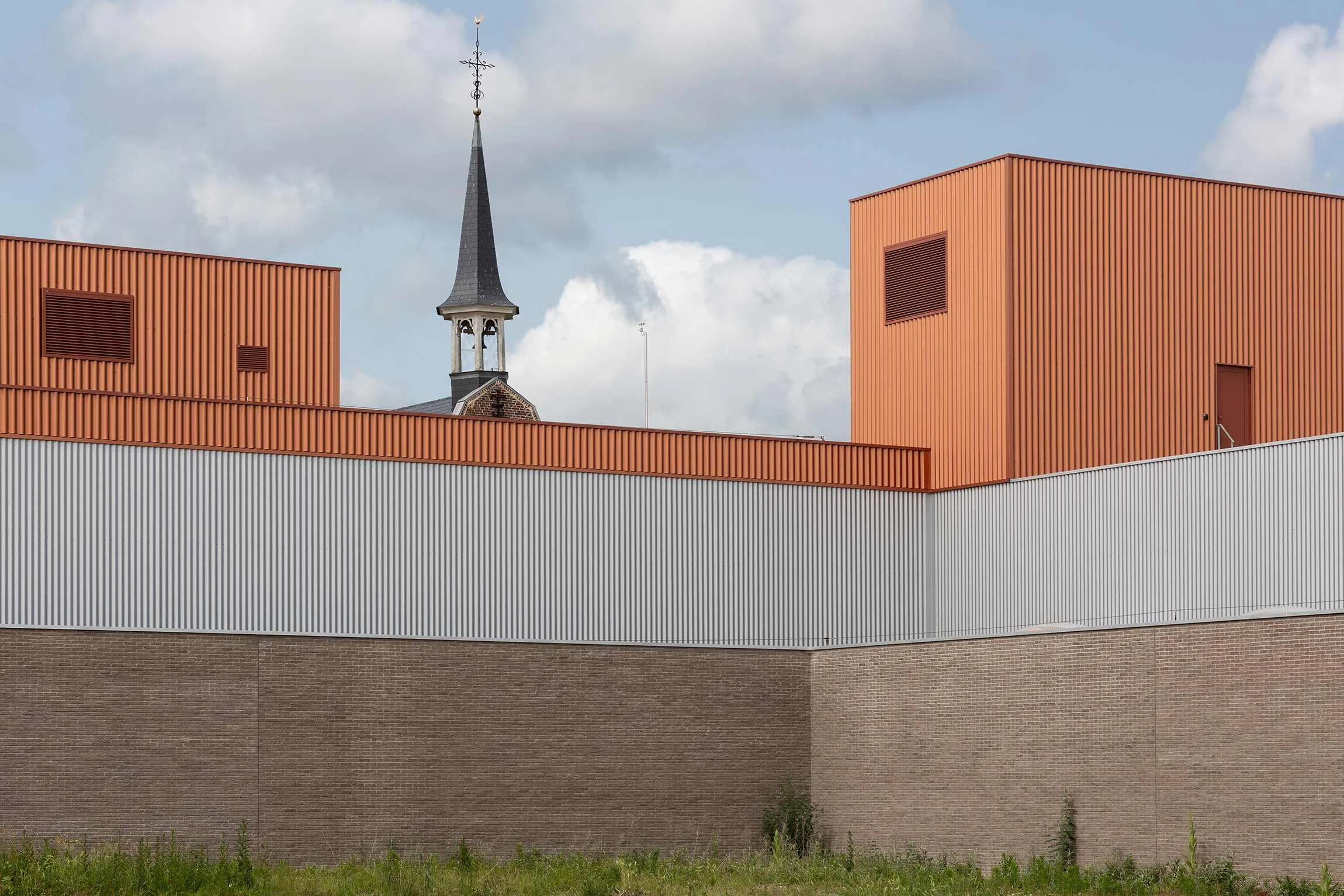 Architecture photography detail of metal facade grey and orange, showing the contrast between the new part of the building and the historic convent chapel repurposed as cultural space.