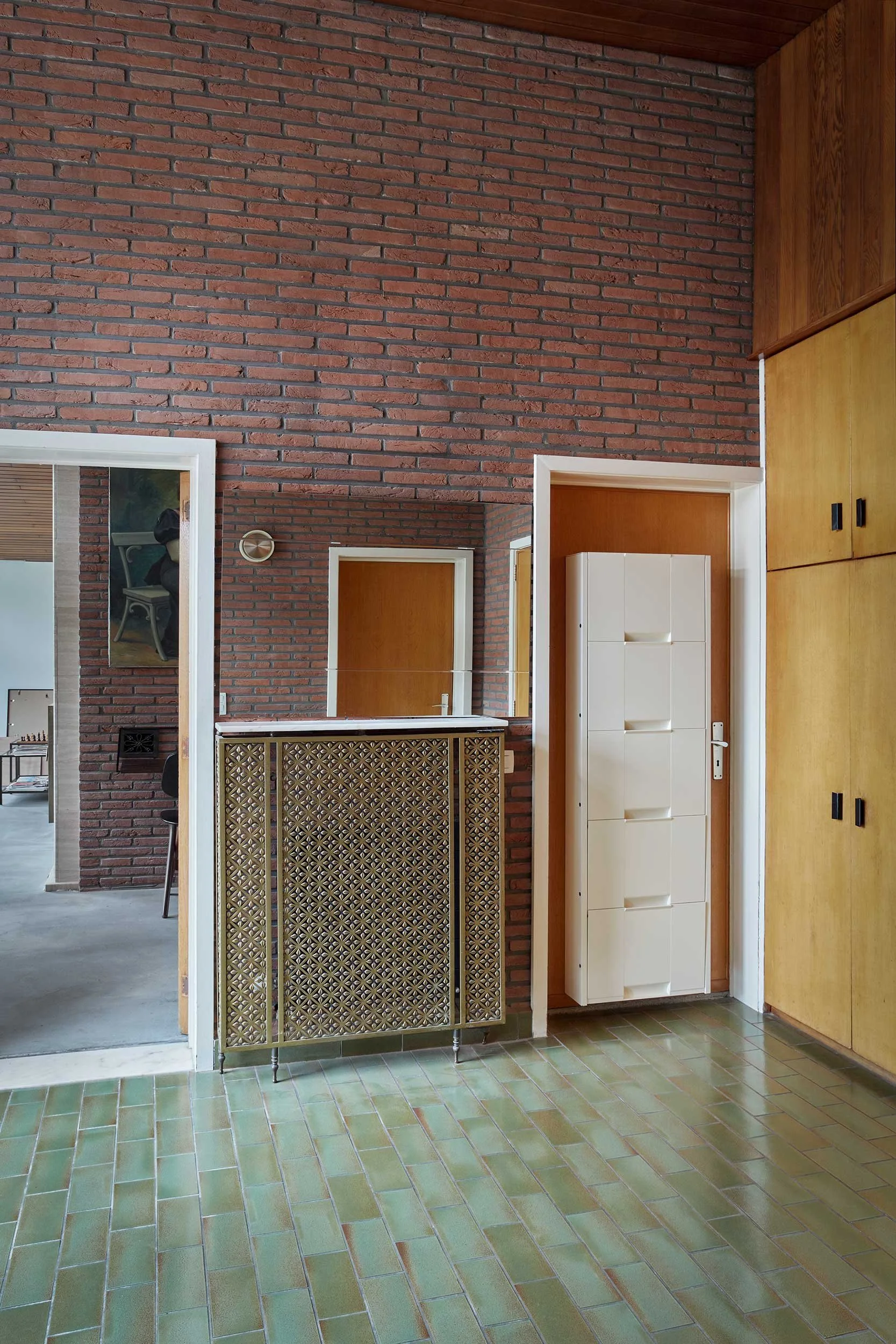 Renovated 1970s interior showcasing green ceramic floor tiles, a brick feature wall, and a vertical shoe cabinet.