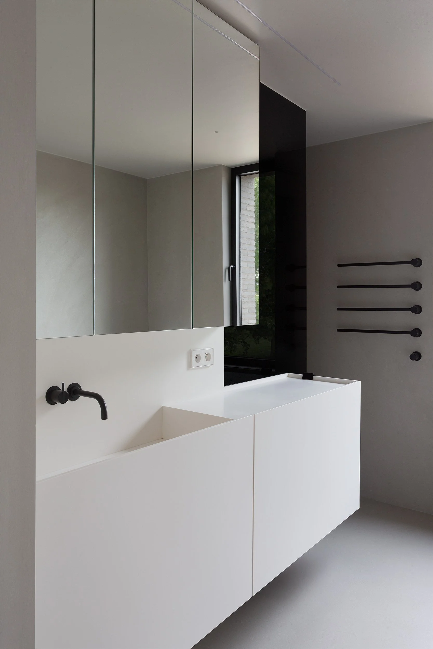 Modern sink area in a private home with a large mirror, beton walls, and Vola matte black fixtures.