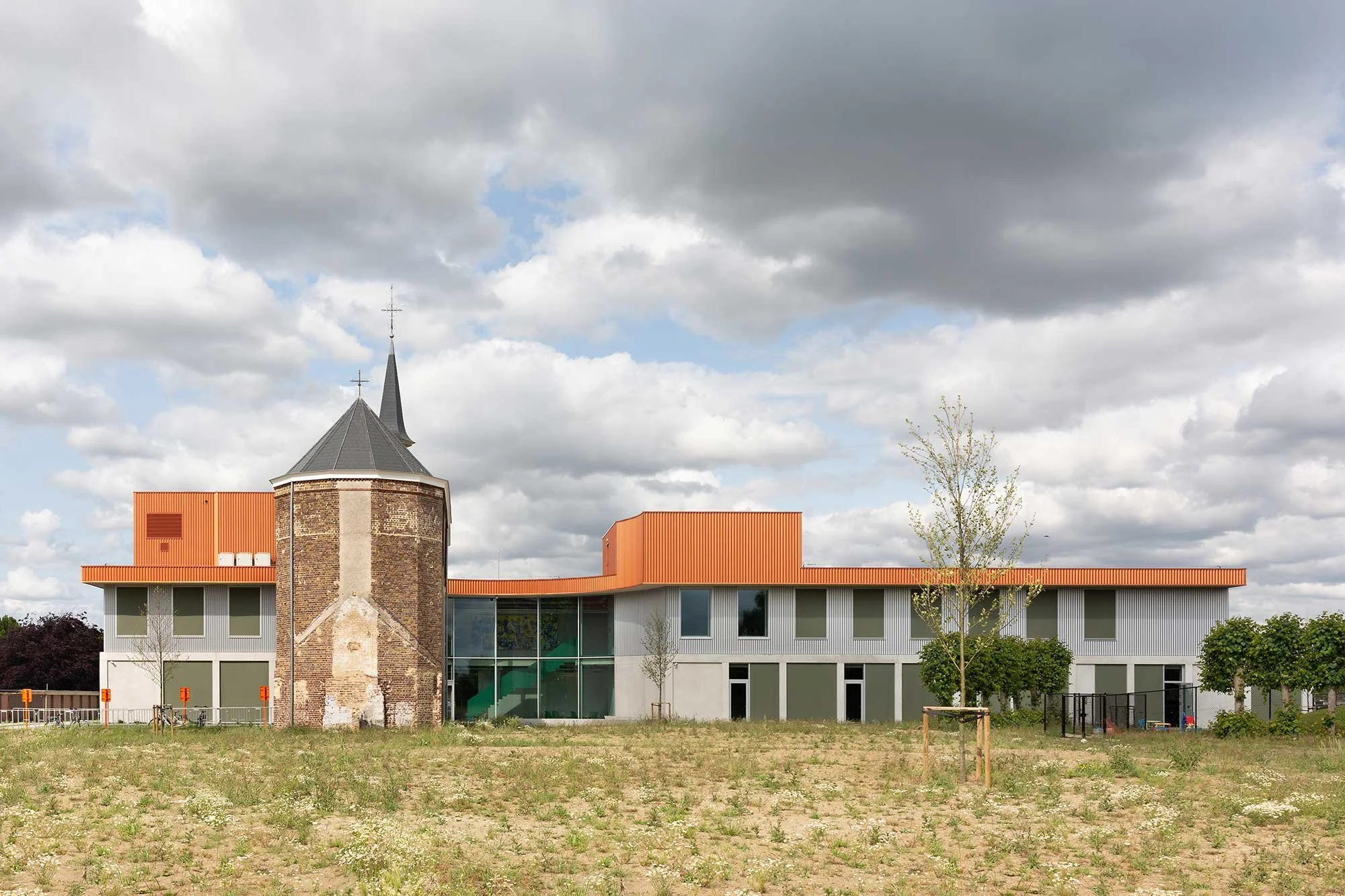 Back side view of the building, under a cloudy sky, showing the contrast between the historic monastery and the new architectural volumes, highlighting adaptive reuse, natural light and the relationship between architecture and landscape.