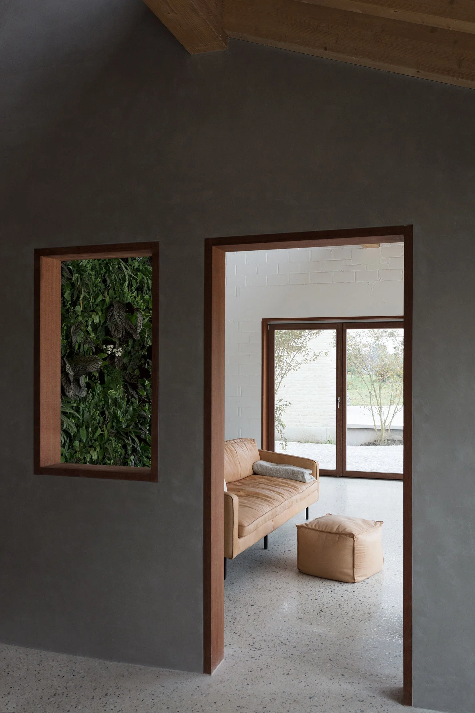 Interior of a renovated house featuring a minimalist living area with terrazzo floor, indoor green wall, natural wood frames, and soft natural light.