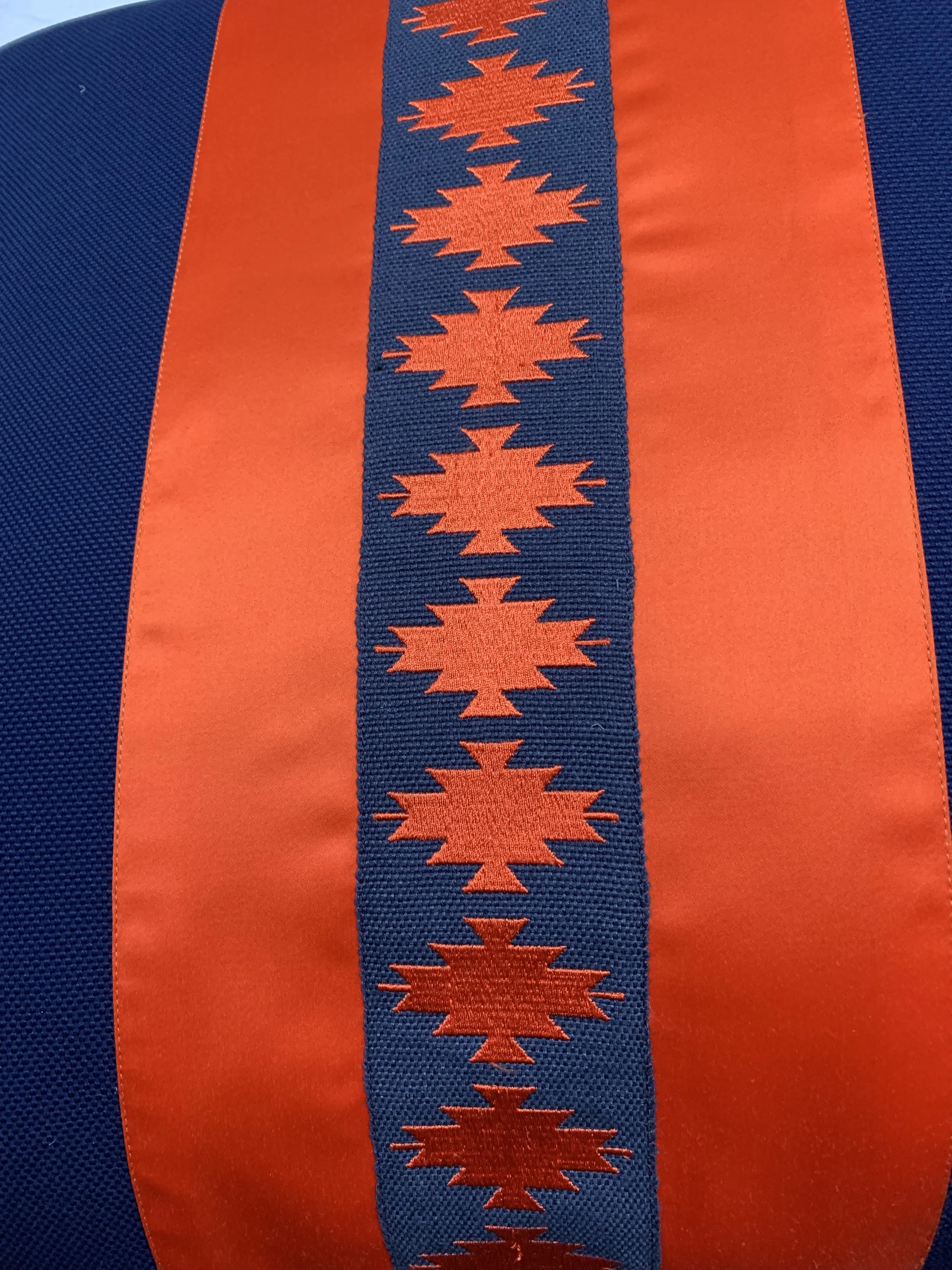Close-up of a textile pattern with orange geometric shapes on a blue background, featuring symmetrical rows and intricate designs.