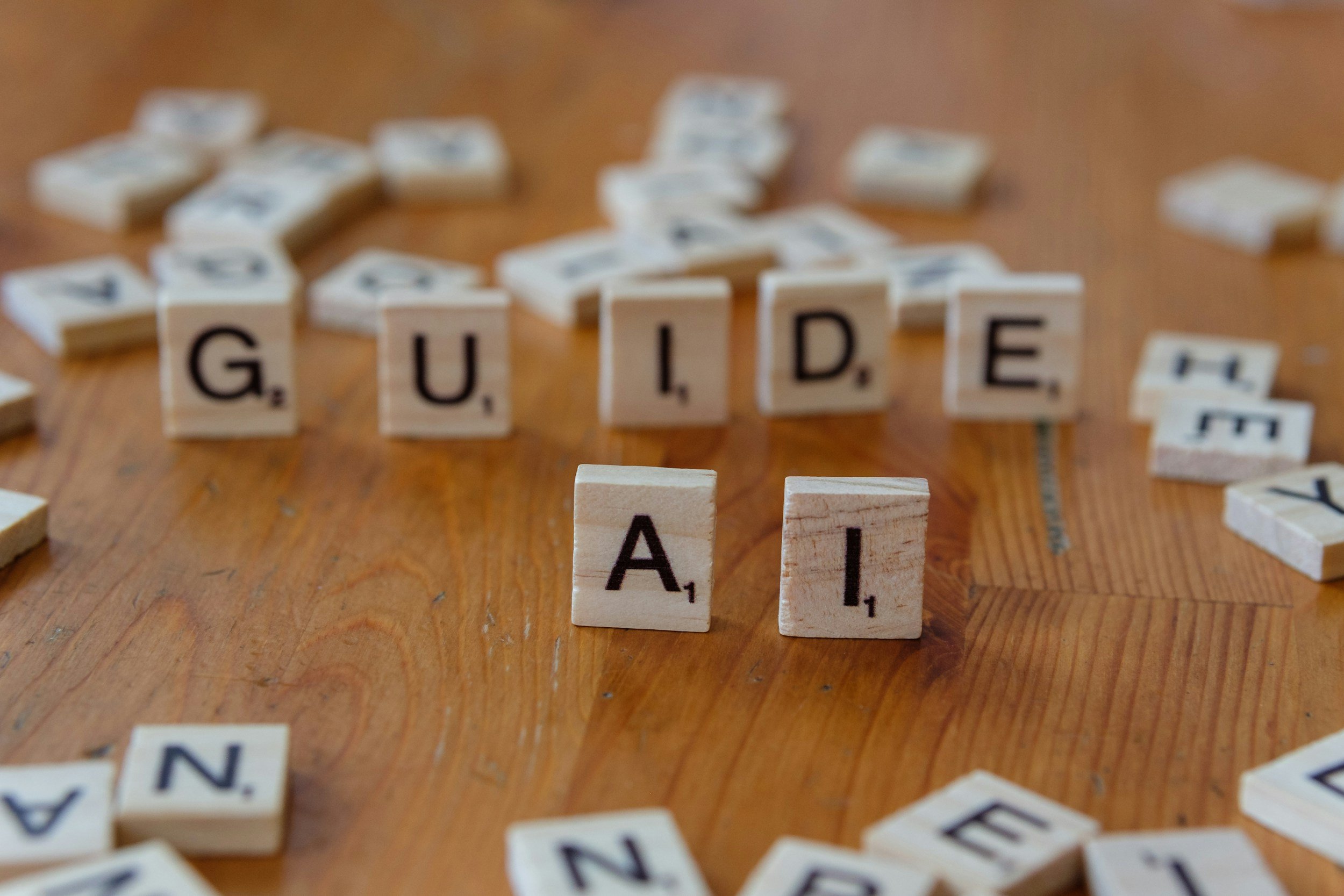 Scrabble tiles spelling out "G. U. I. D. E" on a wooden surface with scattered tiles around.
