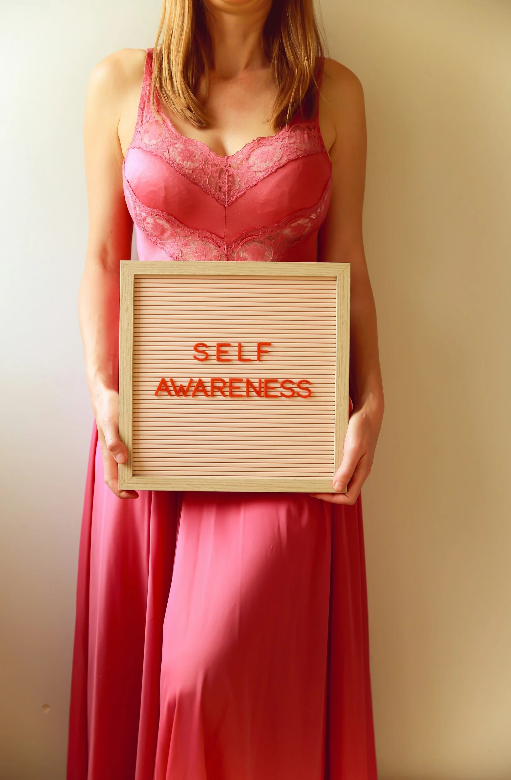 Woman in pink dress holding a sign that says 'Self Awareness' in red letters.