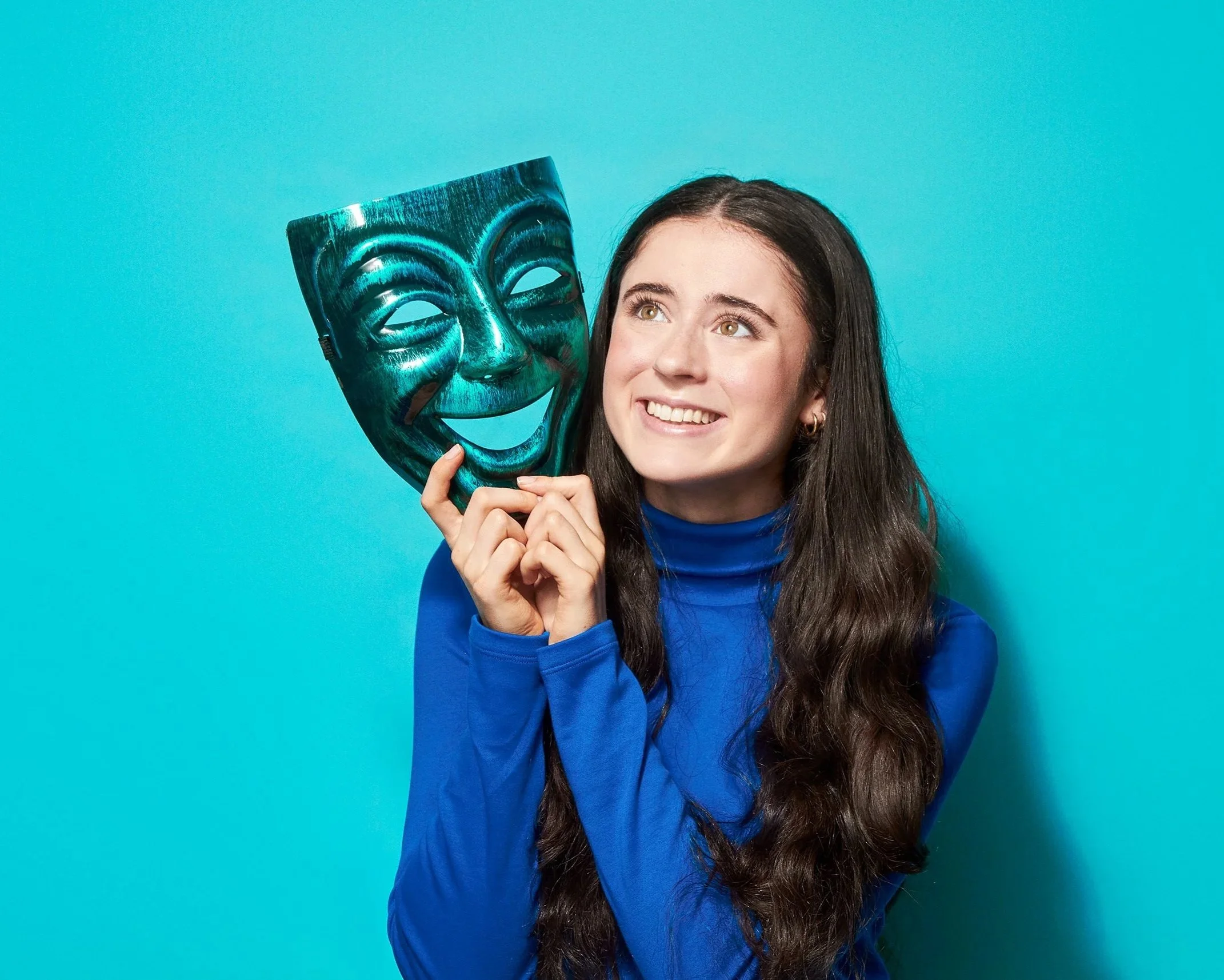 Woman in blue holding a green comedy mask against a blue background.