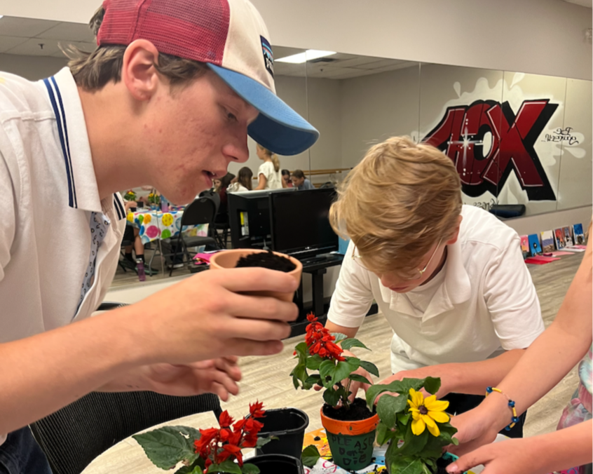 Person with curly hair wearing a clown nose and an orange shirt against a bright blue background.