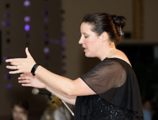 A woman conducting an orchestra or choir, gesturing with her hands.