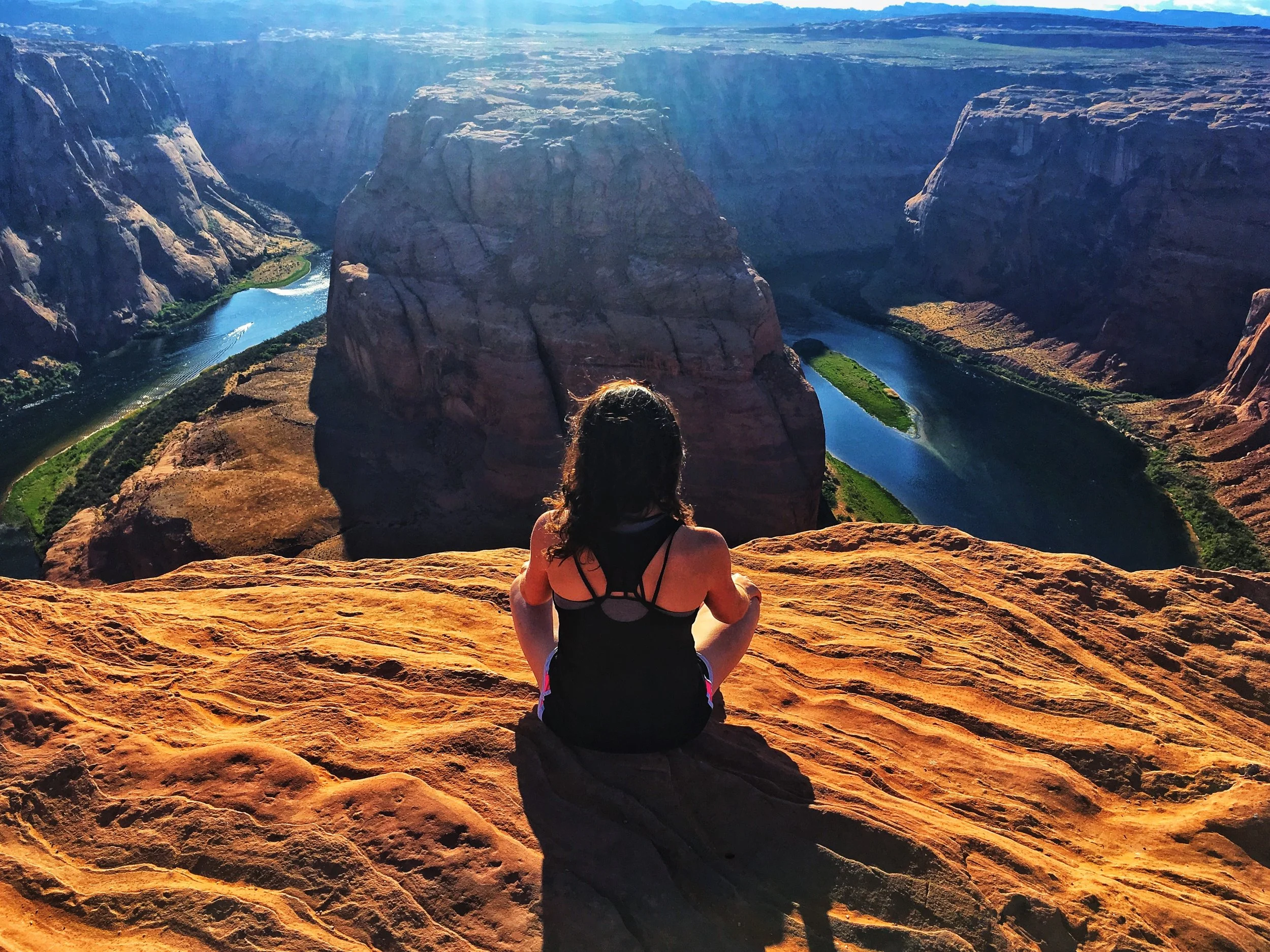 Person sitting on cliff at Horseshoe Bend, overlooking river and canyon, Arizona.