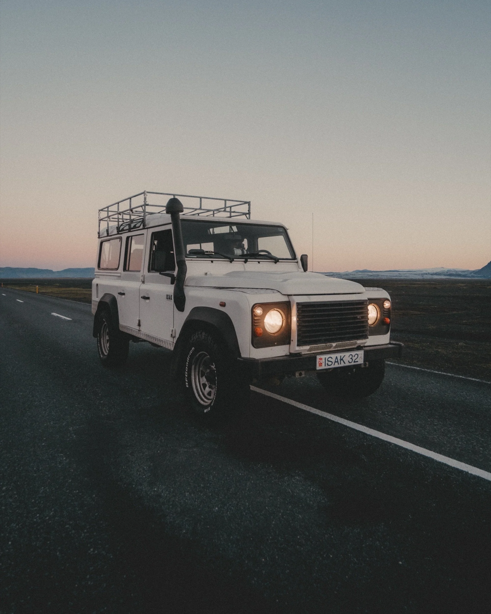 Land Rover Defender on a country road at sunrise with mountains behind, Iceland