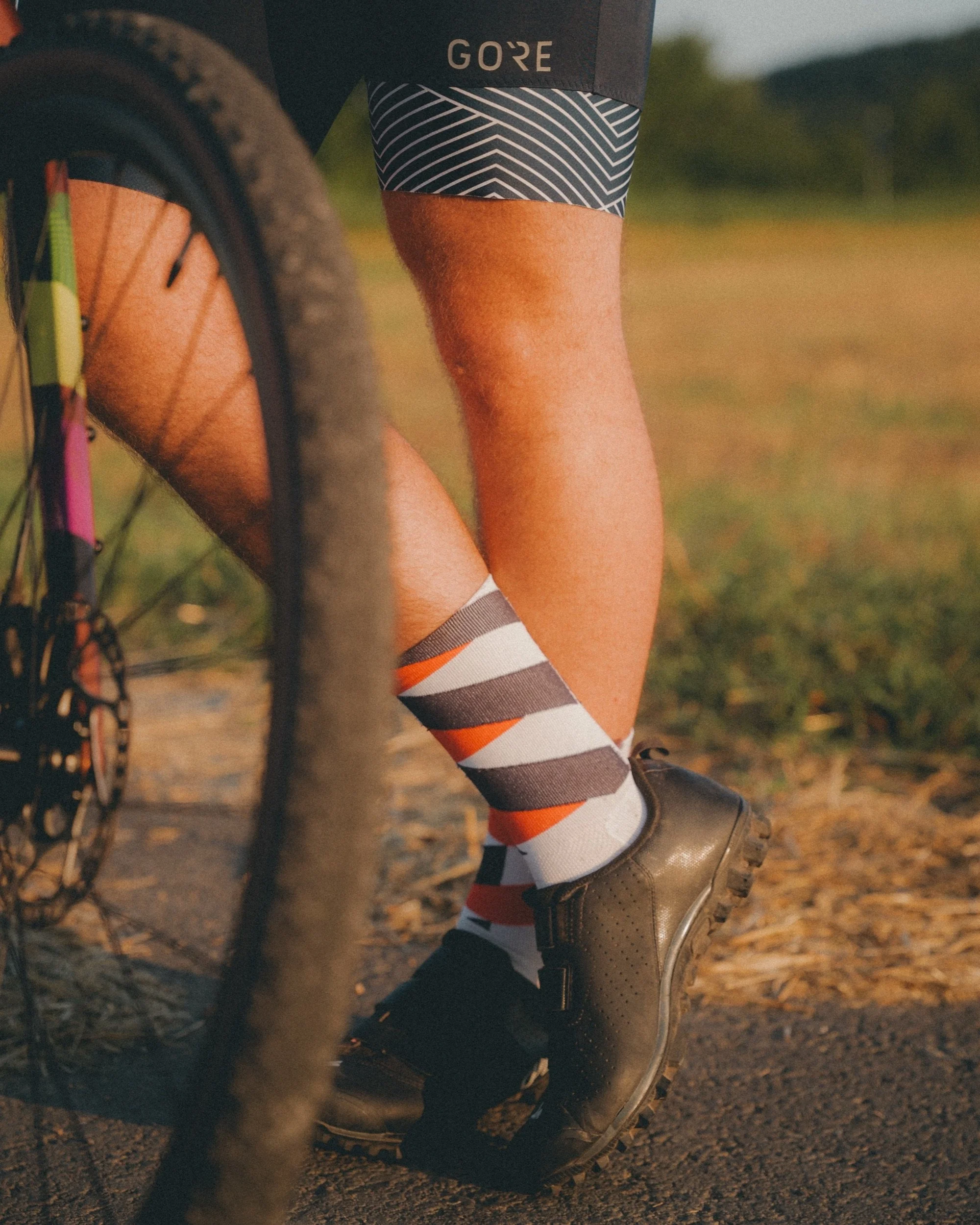 Close-up of cycling shoes and striped socks on a gravel trail, wearing gore wear bibs.