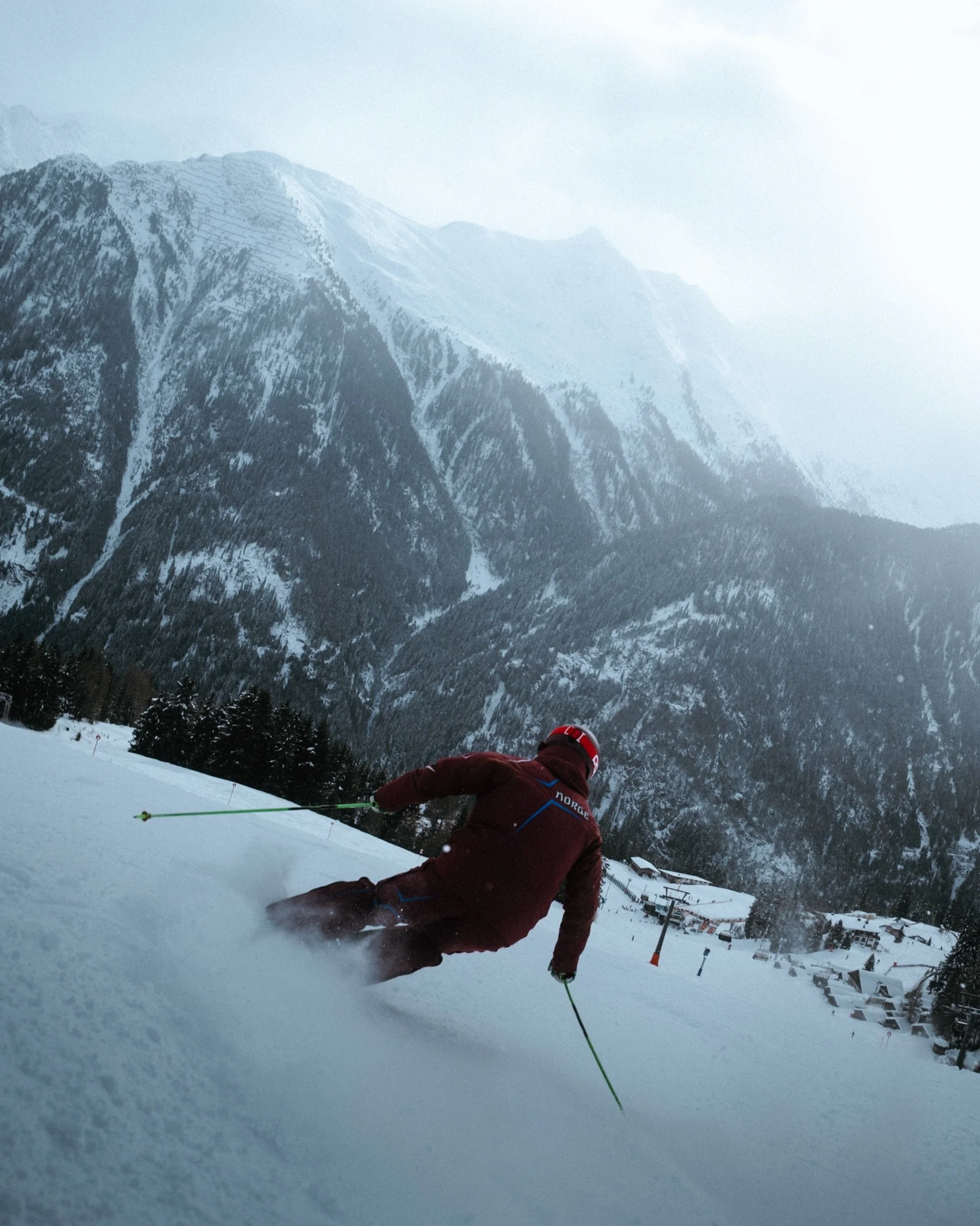 Skier carving below snow-covered peaks, shot while skiing right behind him in Kappl, Austria
