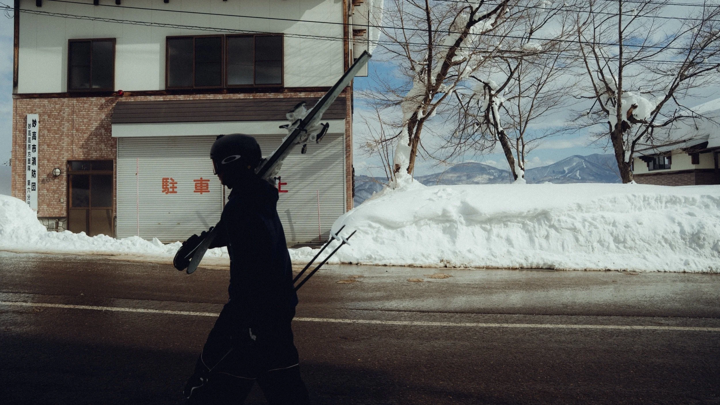 Skier carrying skis along a snowbanked street, Myoko, Japan