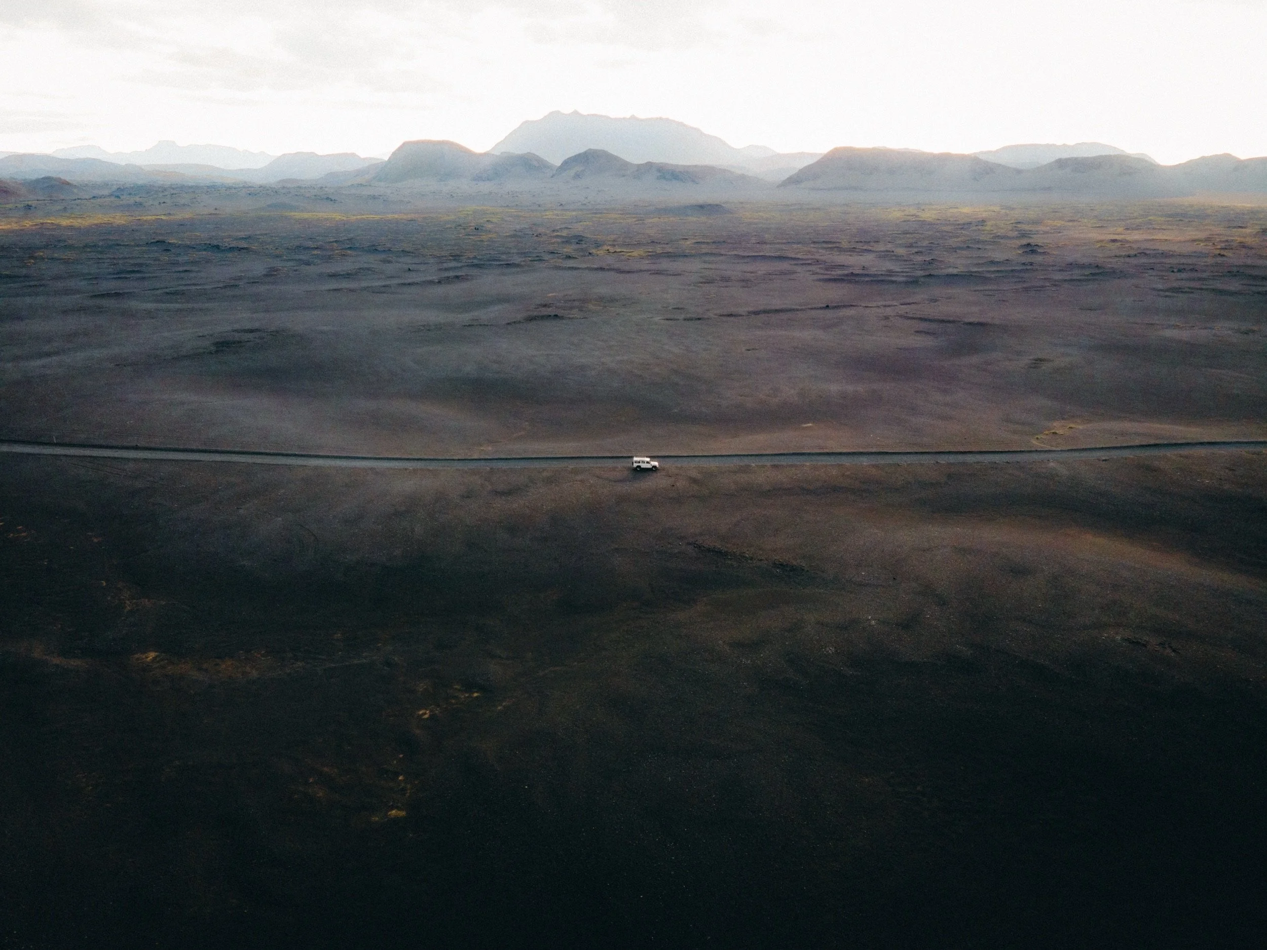 Aerial shot of a Land Rover Defender on a winding road through black volcanic desert, Icelandic Highlands