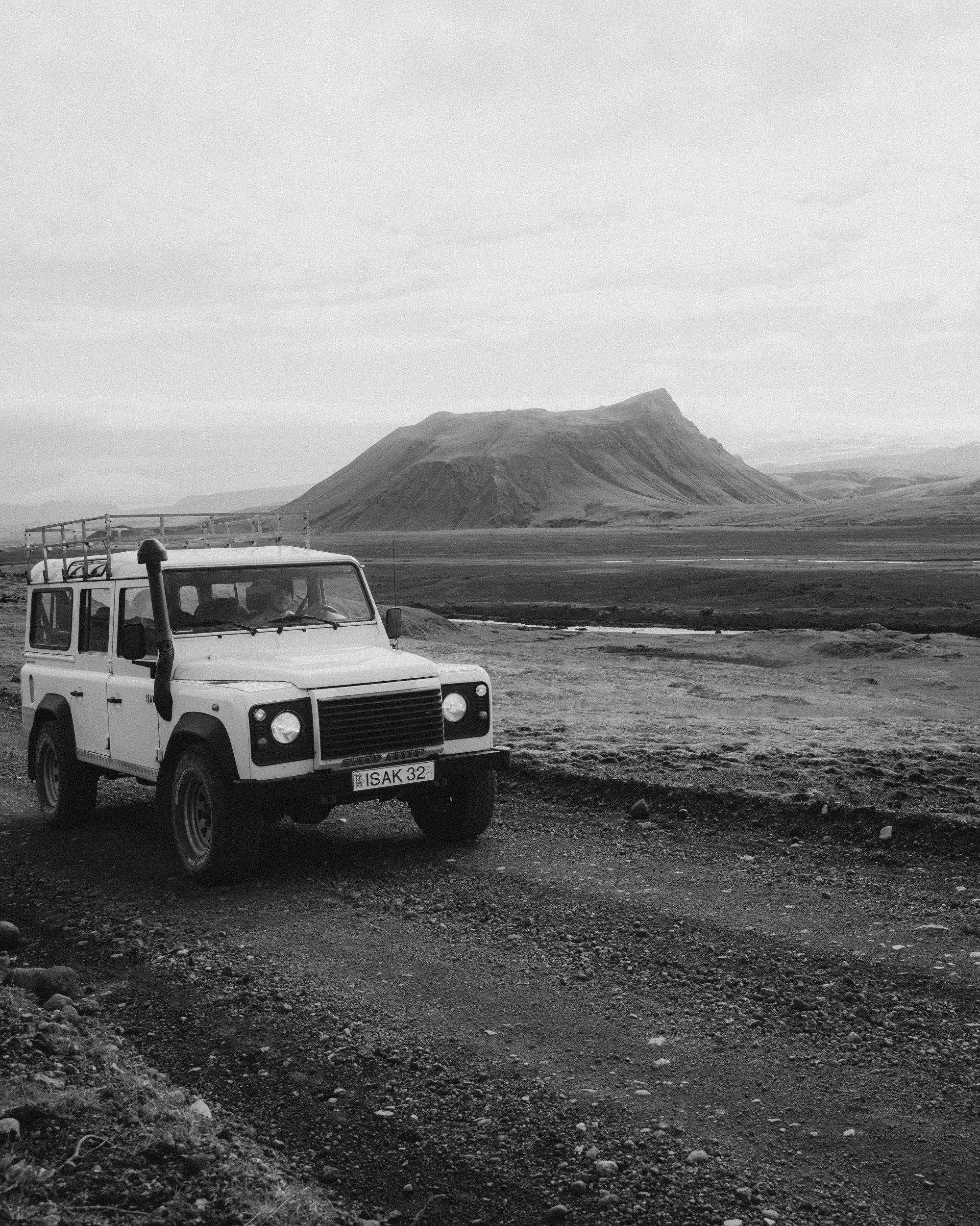 Land Rover Defender on volcanic terrain below a mountain, black and white, Icelandic Highlands