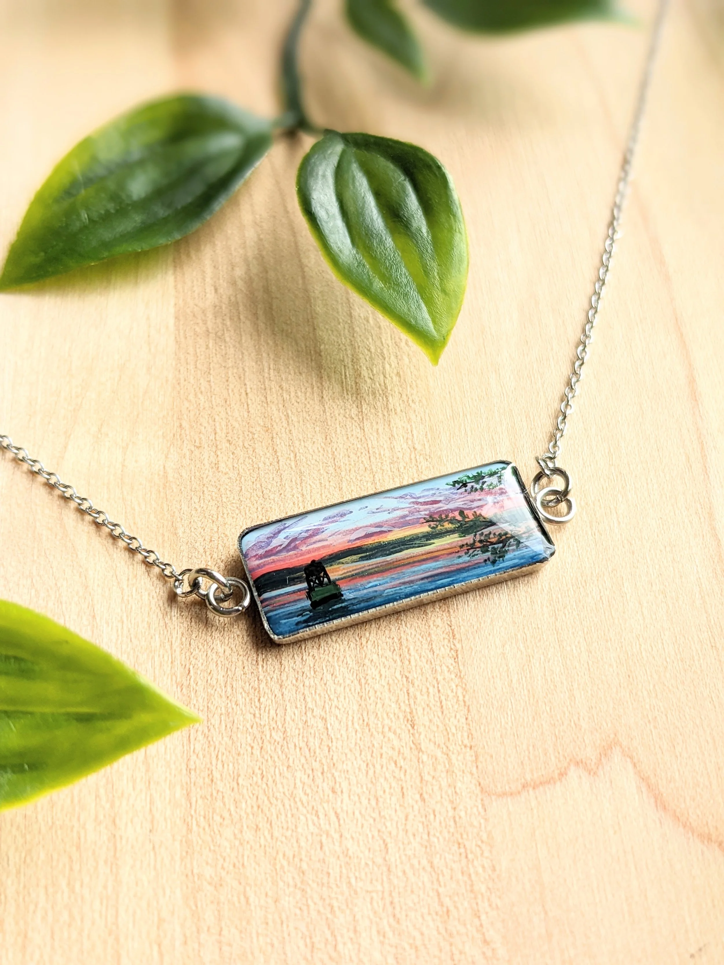 Custom hand-painted bar necklace featuring a lake at sunset and a green buoy