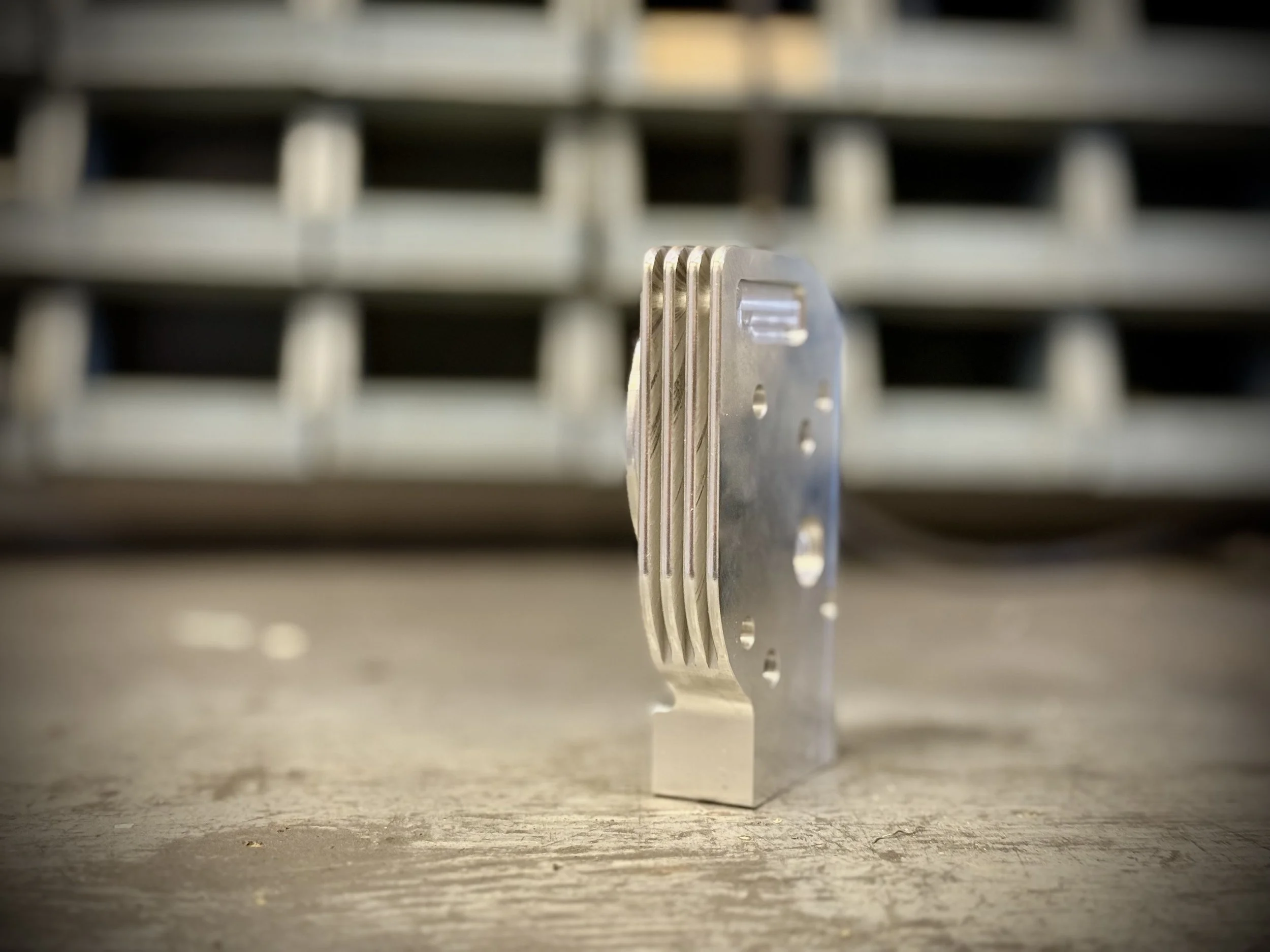 A metallic object with multiple flat, curved layers stacked vertically, standing upright on a textured surface with a blurred background of a metallic rack or shelf.