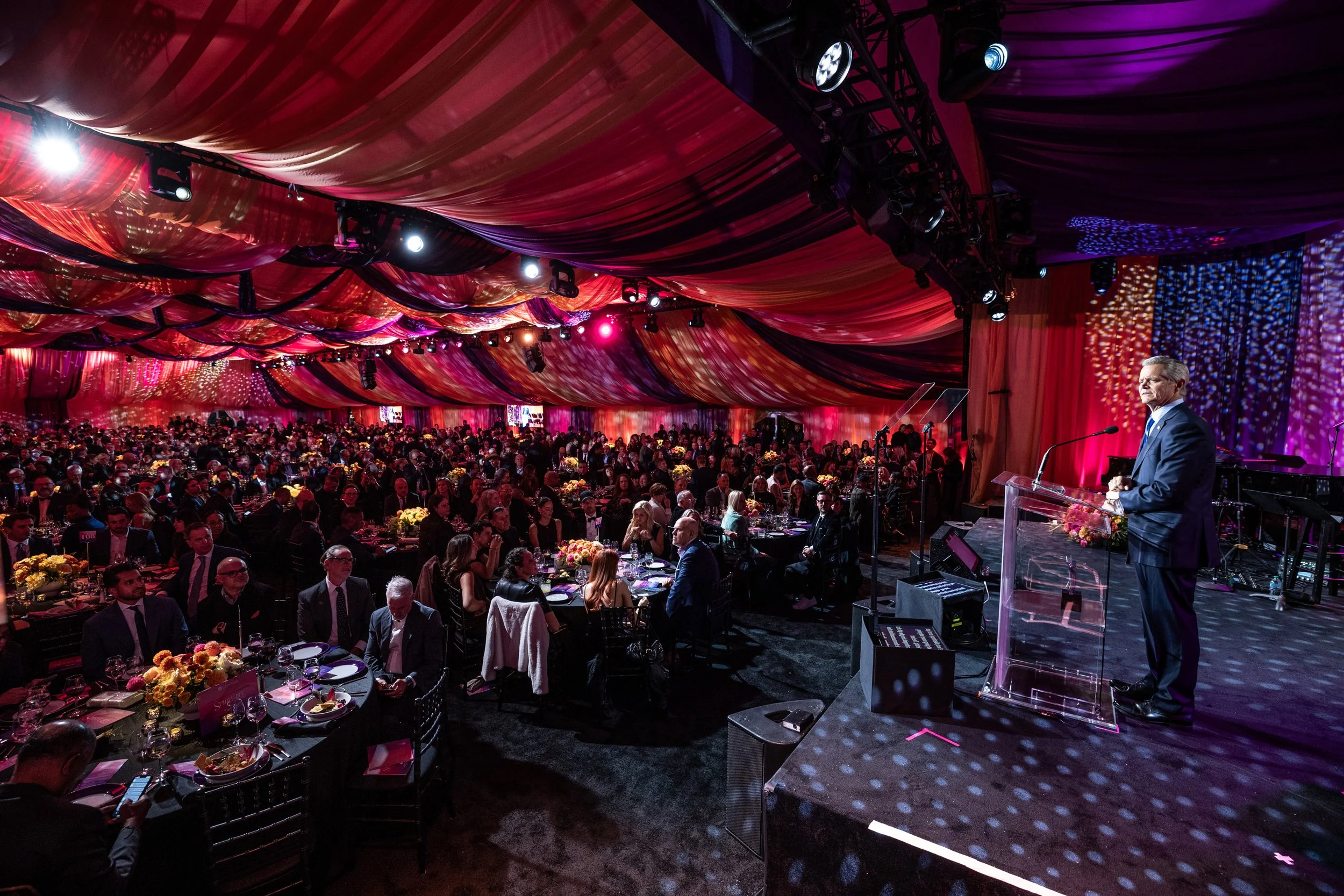 A wide shot of the gala room highlighting the tables, chairs, and décor with guests seated or standing.
