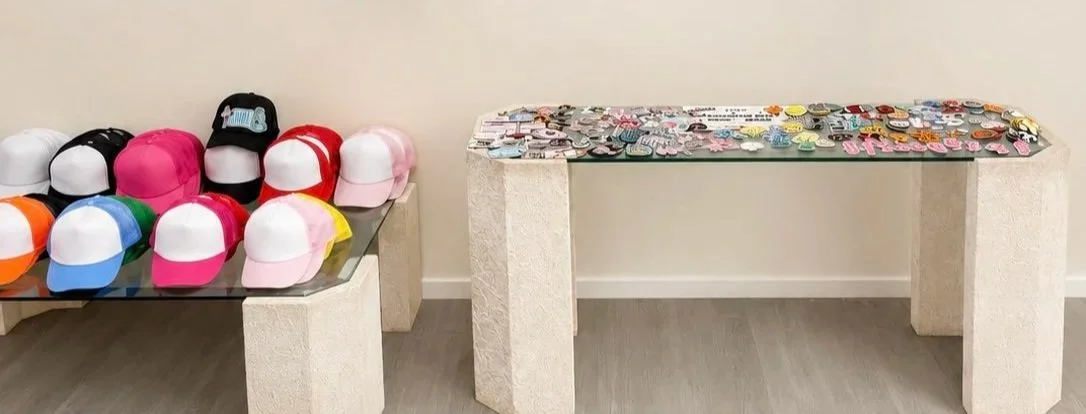 Display of colorful trucker hats on a table and various buttons or pins on a second table.