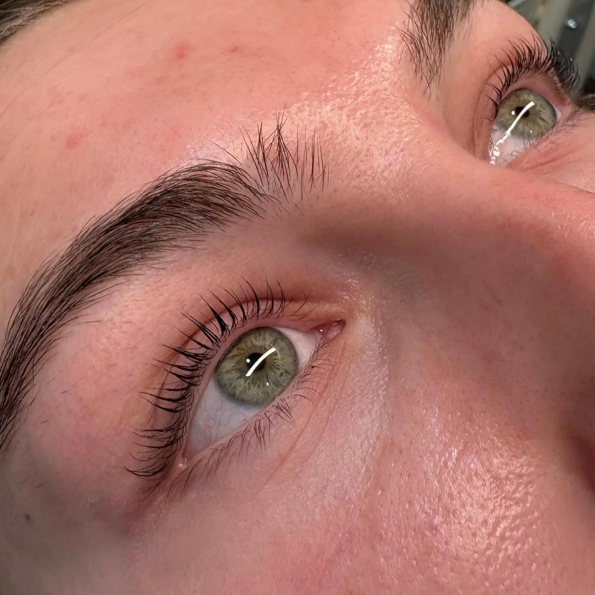 Close-up of a person's eye, eyebrow, eyelashes, and skin with some small blemishes.