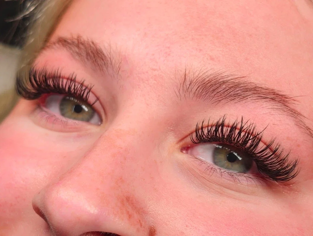 Close-up of a person's face showing their eyes with long, curled eyelashes and well-groomed eyebrows.