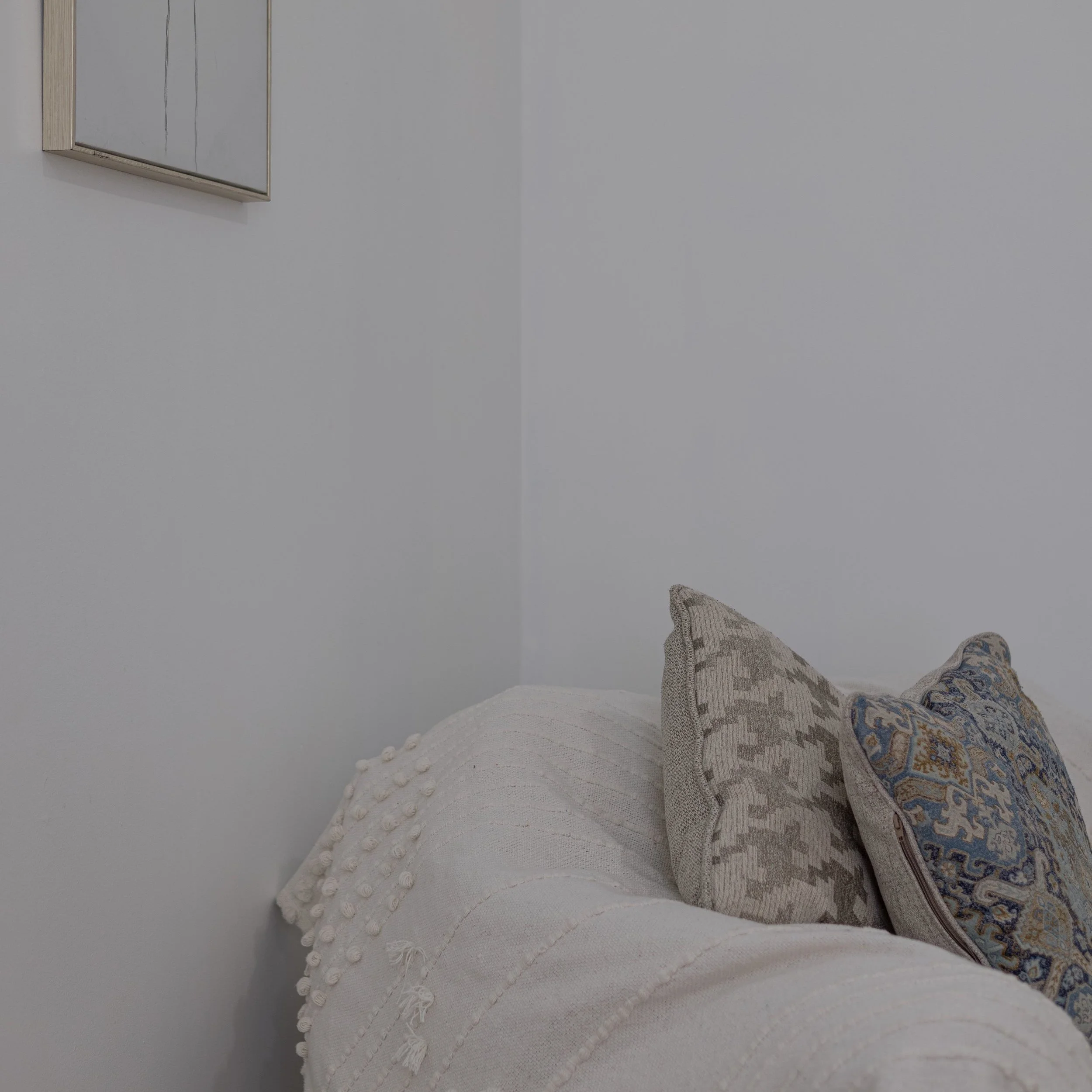 A white couch with textured pillows and a light blanket in a minimalist room.