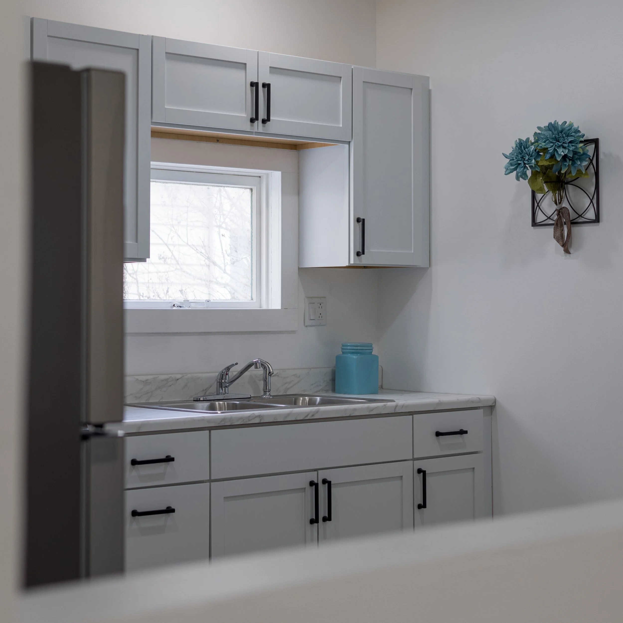 Modern kitchen with white cabinets, a stainless steel sink, marble countertop, window, and decorative blue flowers on the wall.