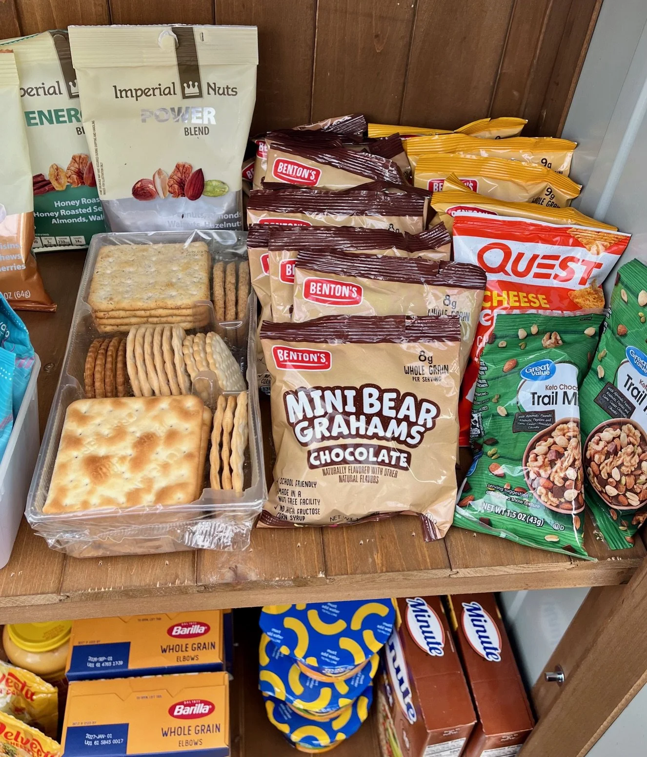 Close-up of pantry shelf with crackers, packaged snacks, trail mix, nuts, and granola snacks.
