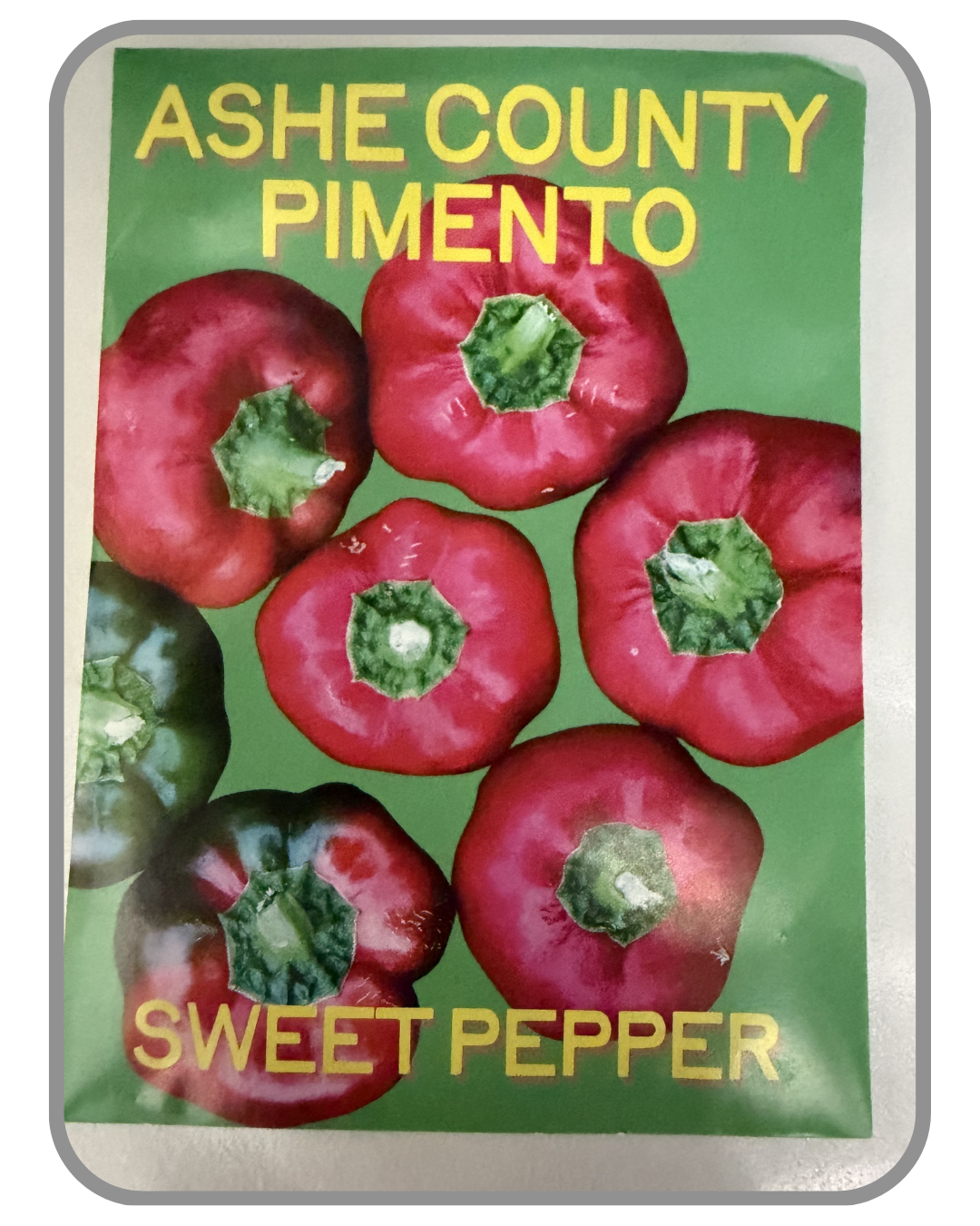 A collection of twelve heirloom seed packet images featuring vegetables grown by farmers and seed stewards in Western North Carolina. Each packet displays a close-up photograph of the crop variety and its name. The varieties include Blue Goose Southe