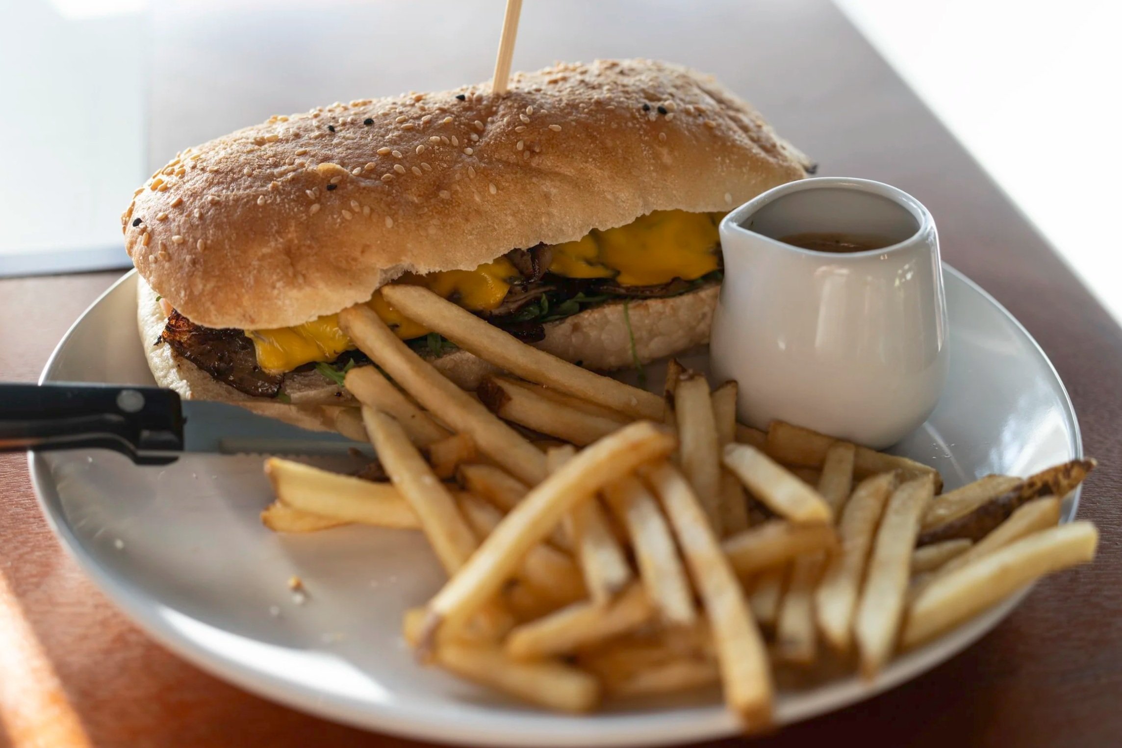 Cheesesteak sandwich with fries and sauce on white plate