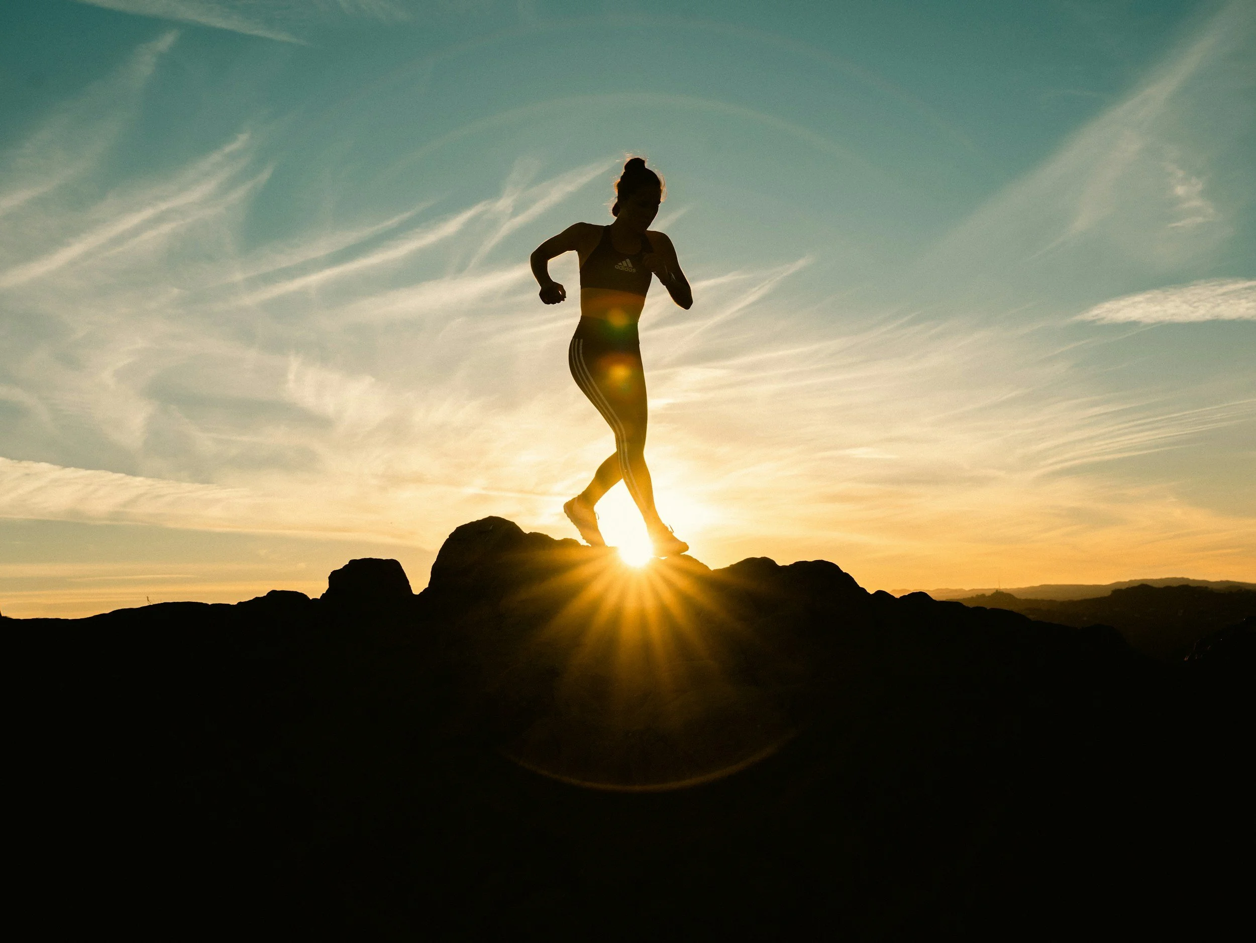 Silhouette of a person running on a rocky terrain at sunset with a clear sky and some clouds.