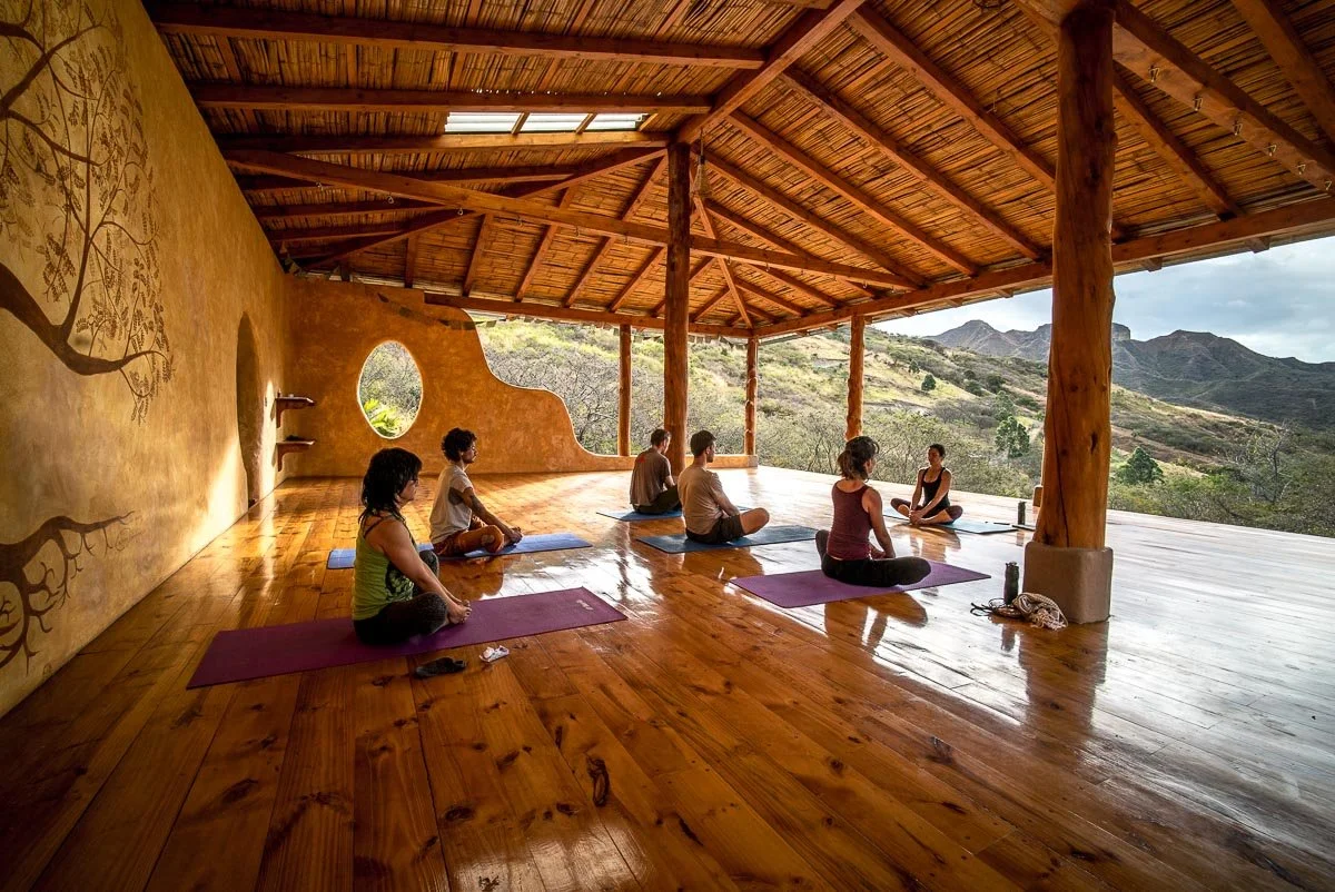 People practicing yoga on mats in a wooden studio with open walls showing a mountain landscape