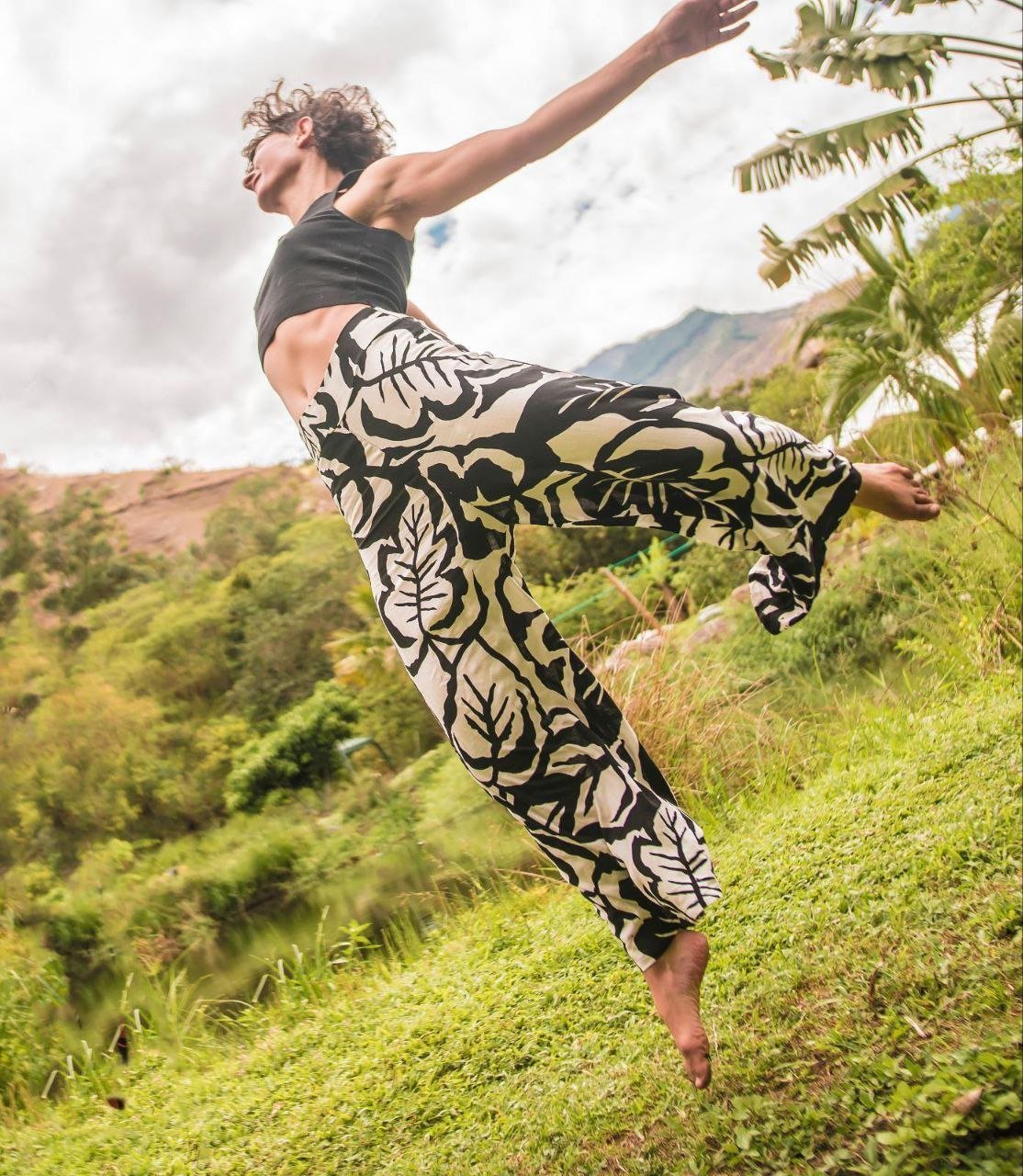 Person jumping and dancing outdoors in a green landscape with mountains and cloudy sky in the background.