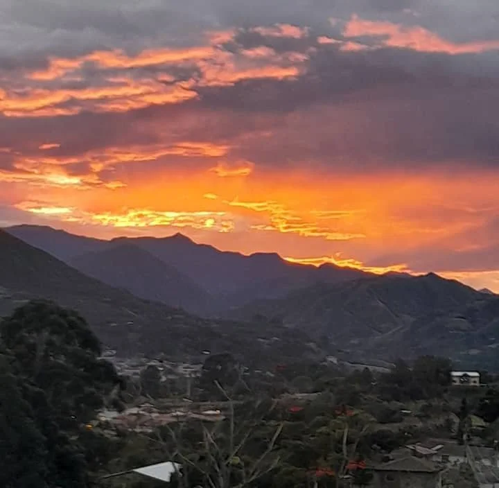 Scenic sunset over mountains with orange and purple clouds, view of a town and trees in the foreground.