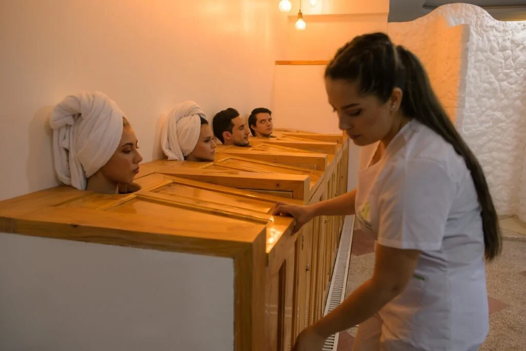 People with towels on their heads in wooden lockers, receiving massages from a spa attendant