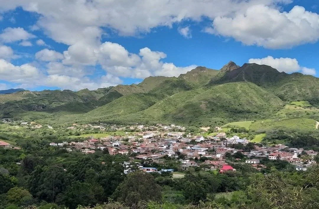A town nestled among green hills and mountains under a partly cloudy sky.