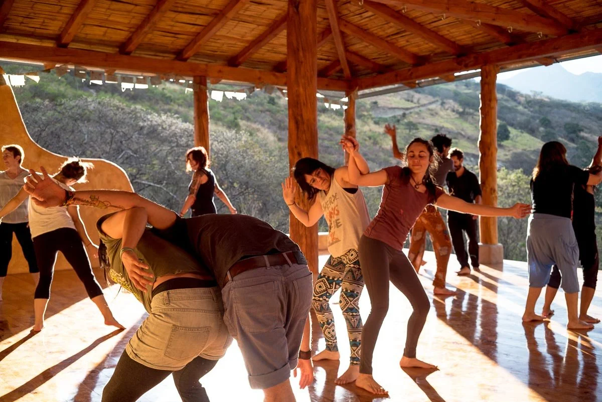 Group of people dancing on a wooden deck with a mountain landscape in the background during daytime.