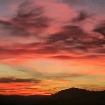 Colorful sunset with orange, pink, and purple clouds over a dark silhouette of hills.
