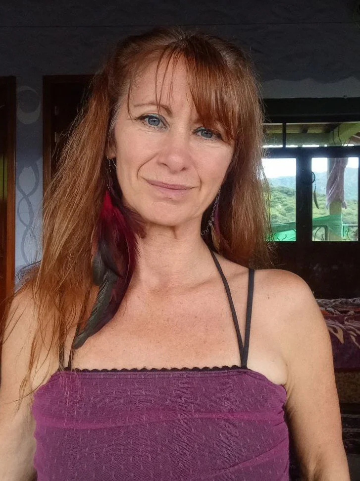 Asha Christiansen, founder of Awakening Vacations, standing indoors with greenery visible through a window.