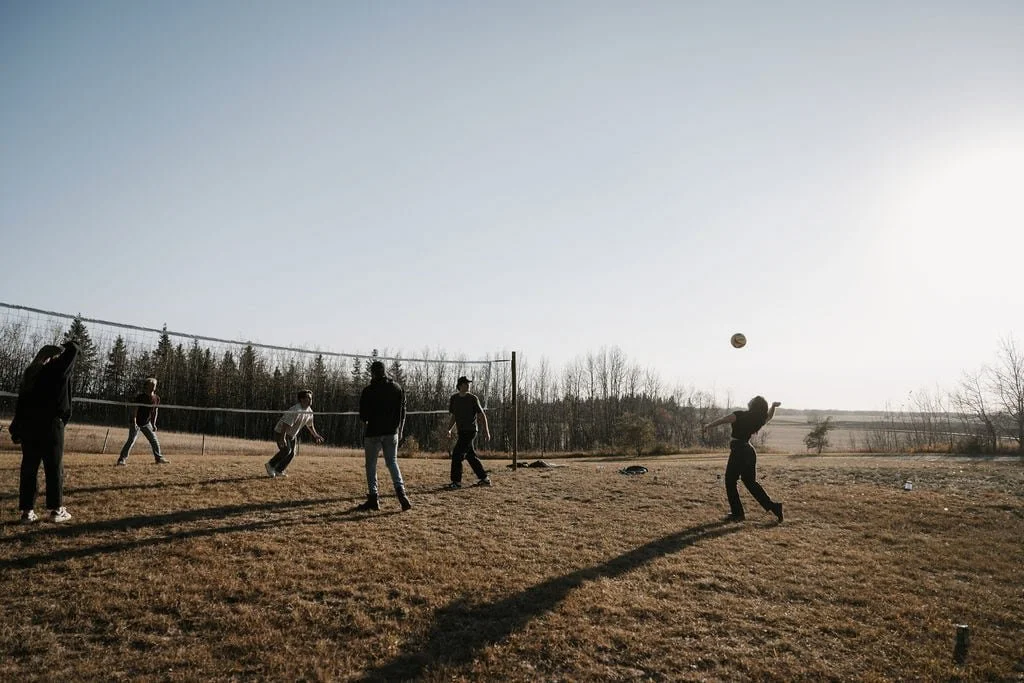 Group of friends playing volleyball on a grassy field at sunset, highlighting a serene, retreat-like atmosphere with a boho spirit, perfect for outdoor enjoyment and relaxation.