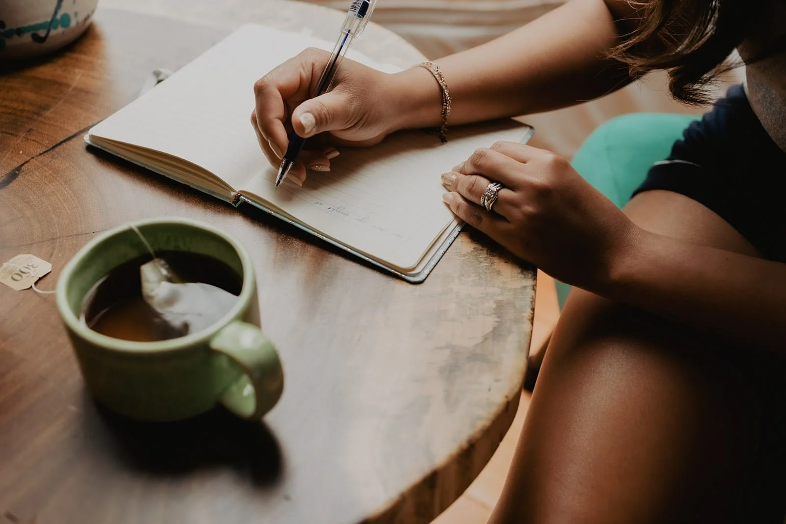 Close-up of a hand writing in a journal on a wooden table, with a steaming cup of tea nearby, capturing a serene and reflective moment within the peaceful geodome retreat.