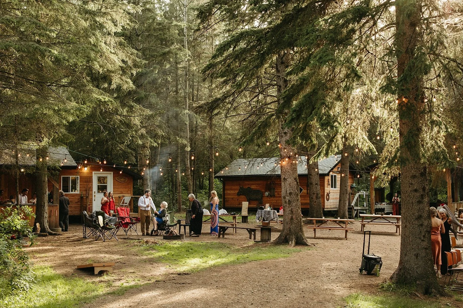 Picturesque wedding venue nestled in a woodland setting with charming cabins, string lights, and guests mingling, creating a warm and inviting retreat atmosphere perfect for a boho celebration.