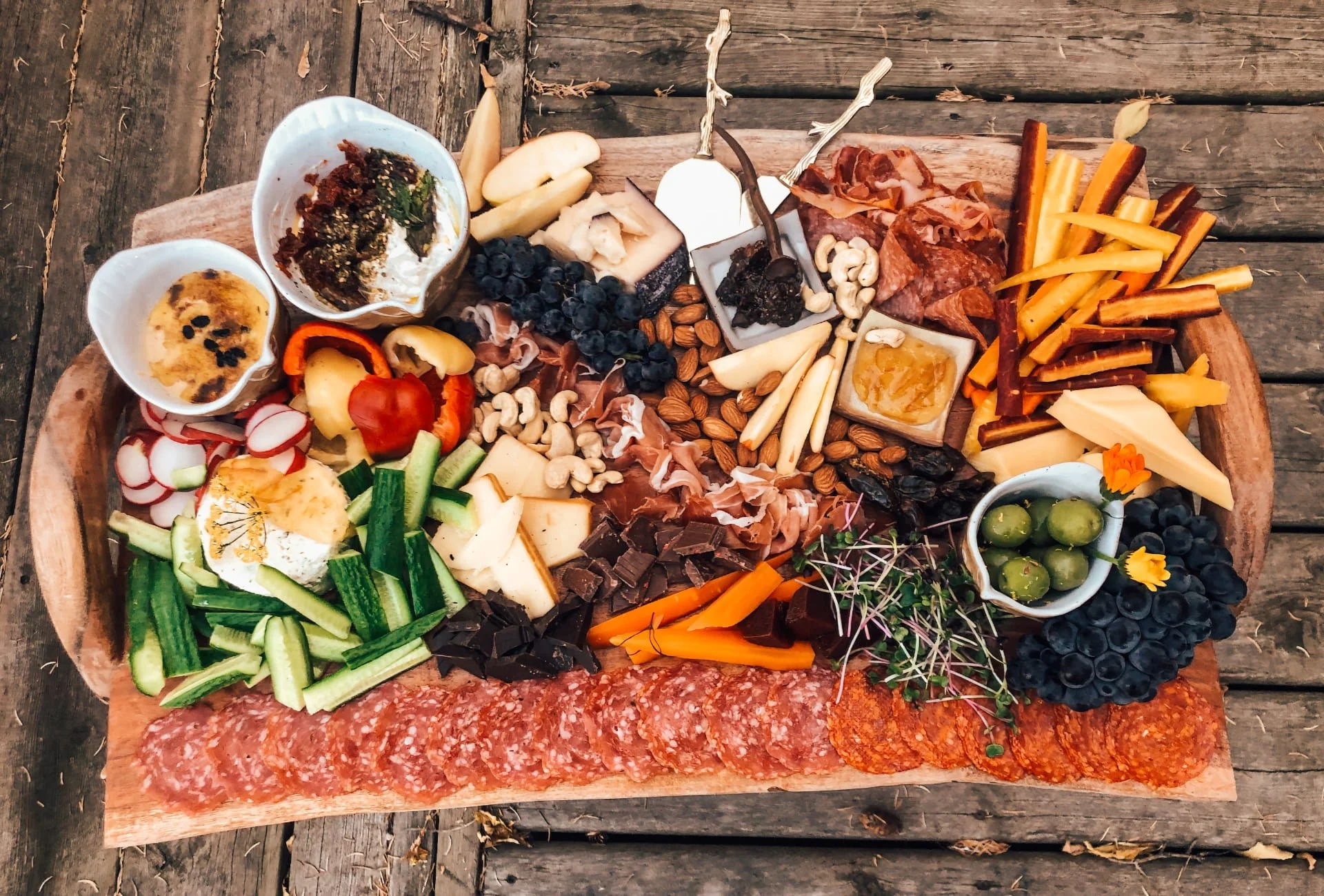 A lavish charcuterie spread on a wooden board featuring an array of cheeses, meats, nuts, and fresh vegetables. The rustic setup and vibrant colors create a cozy, retreat-like dining experience.