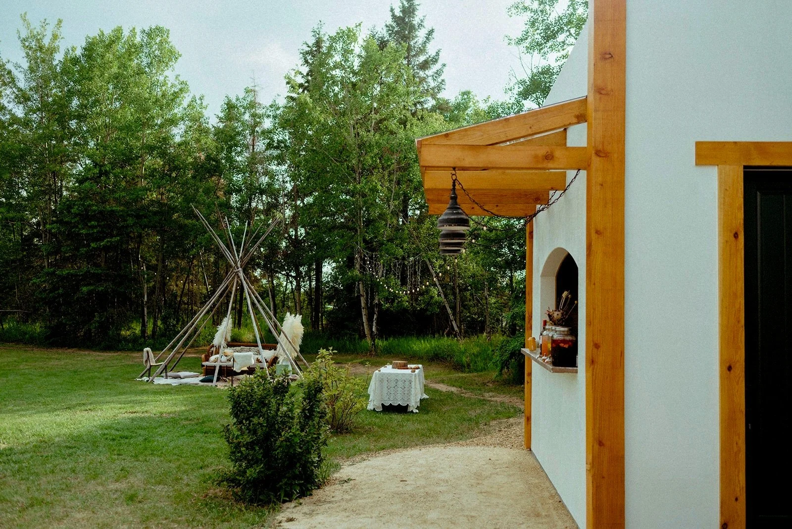 Boho outdoor bar setup with drink dispensers filled with colorful beverages and an array of canned drinks, all arranged on a rustic countertop with a forest backdrop.