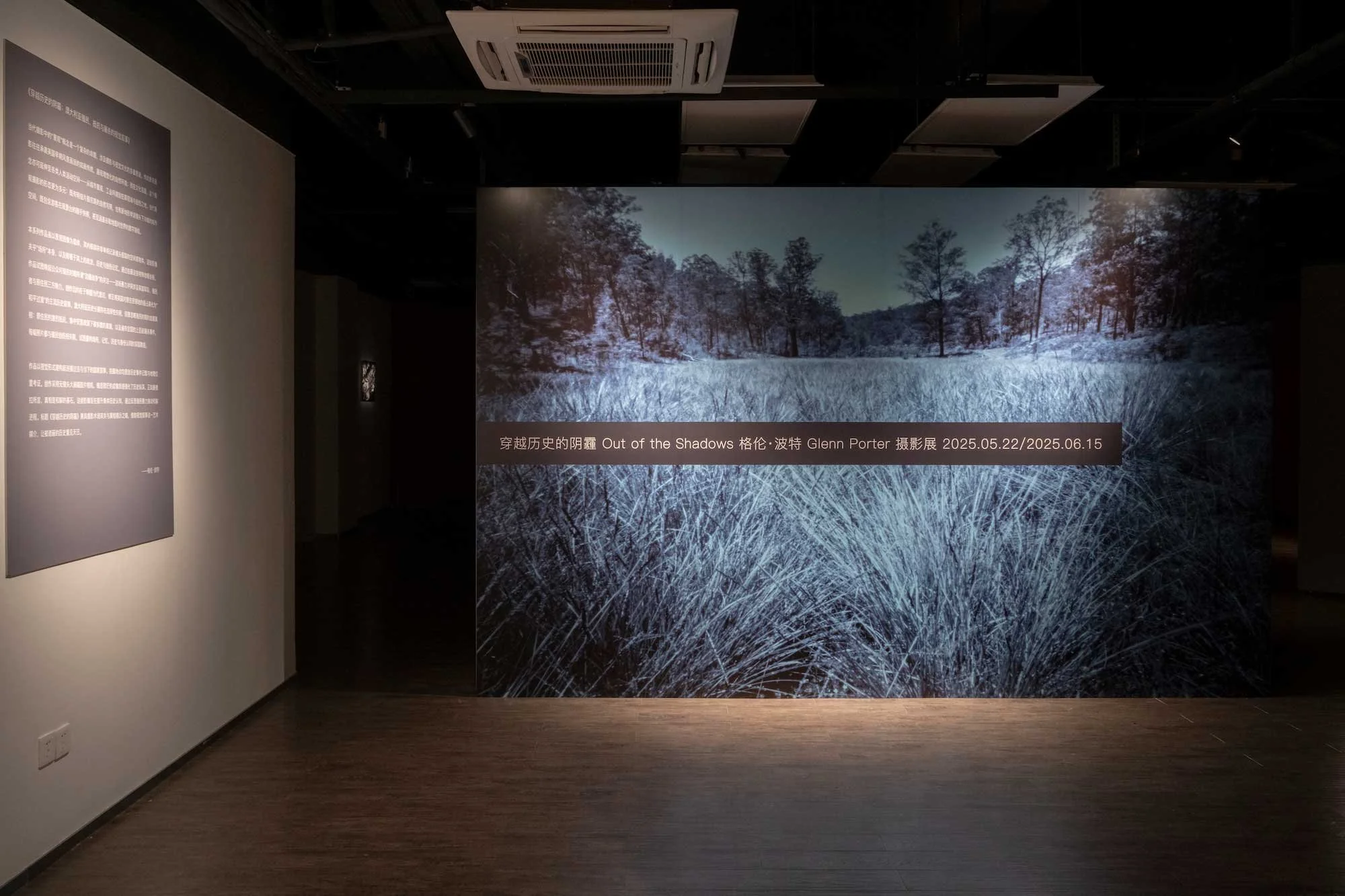 An art exhibition display featuring a large photograph of a natural landscape with tall grass and trees in the background, along with a text caption in Chinese and English about the artist Glenn Porter, dated May 22, 2025, to June 15, 2025.