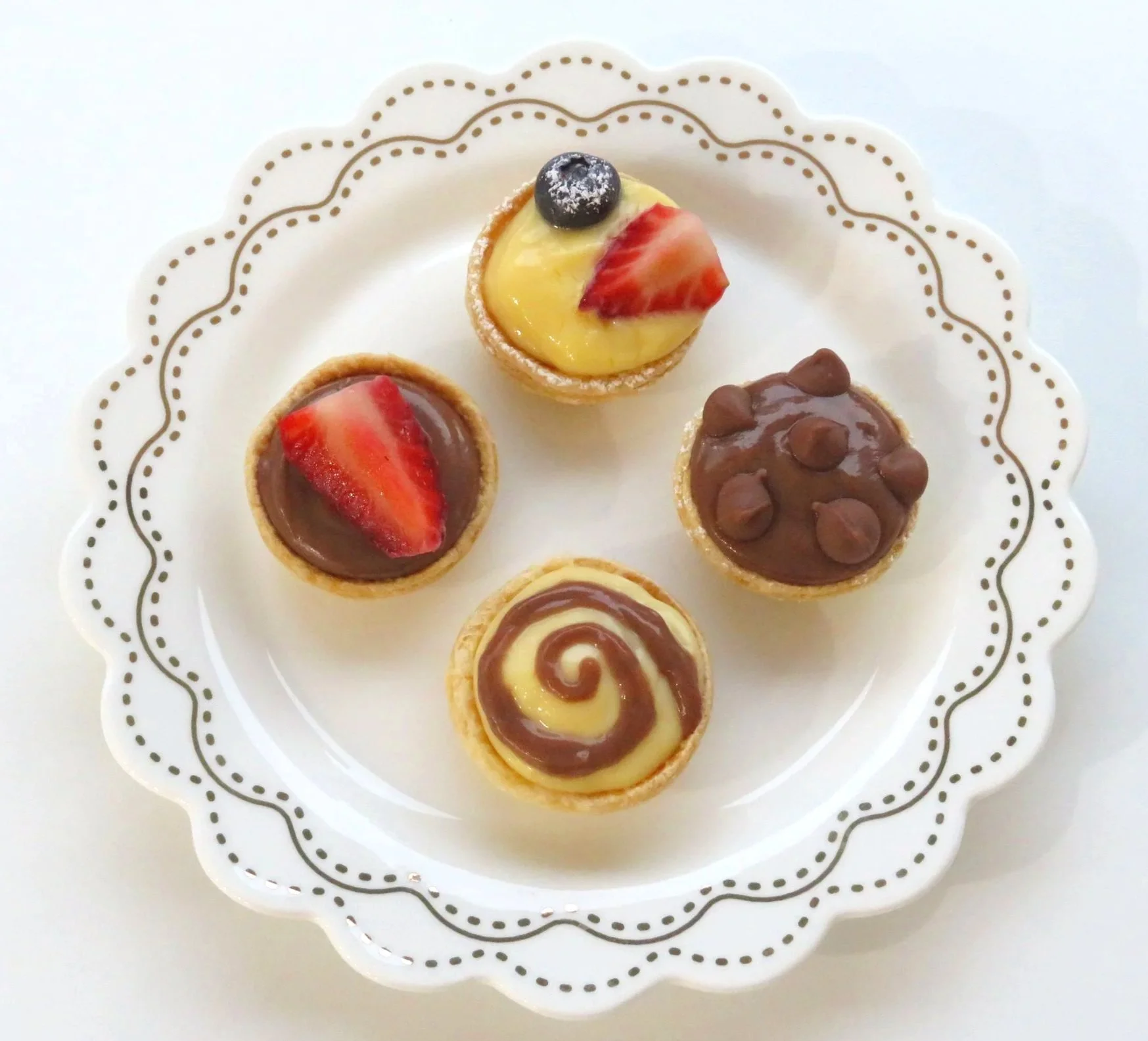 Four Mini Custard Tarts including chocolate and vanilla swirl on small plate with fresh berries and choc chips
