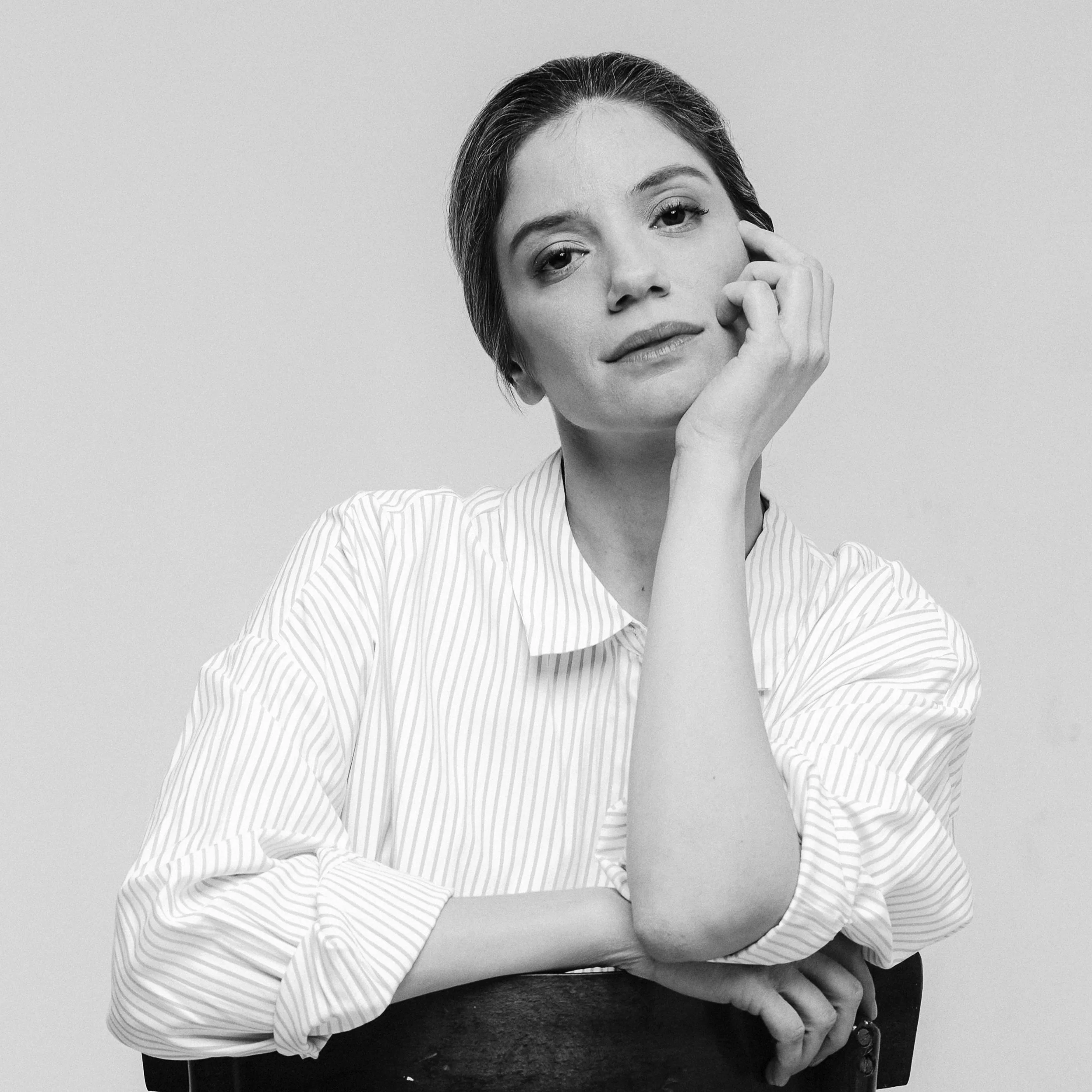 A woman with short hair wearing a striped shirt, resting her head on her hand, looking at the camera.