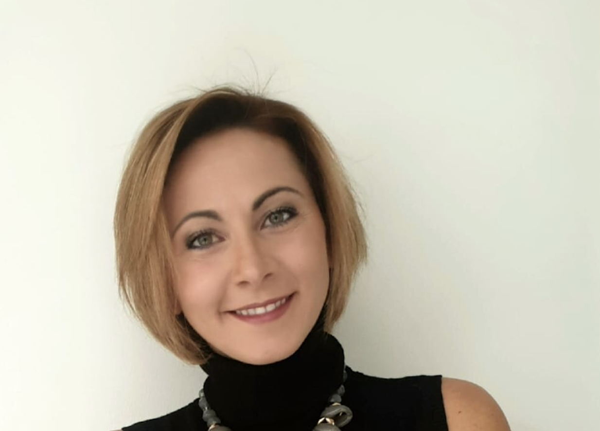 A portrait of a woman with short brown hair, wearing a black turtleneck sweater, smiling against a white background.