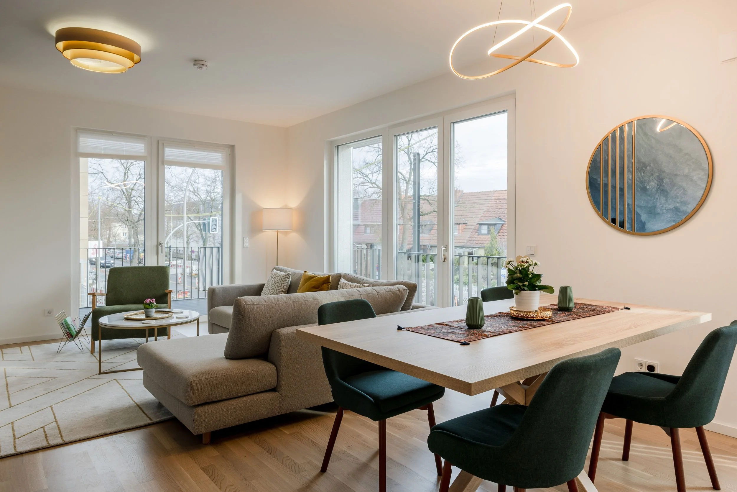 Bright open-plan living and dining room with L-shaped sofa, round mirror, and pendant lighting by Akiva.